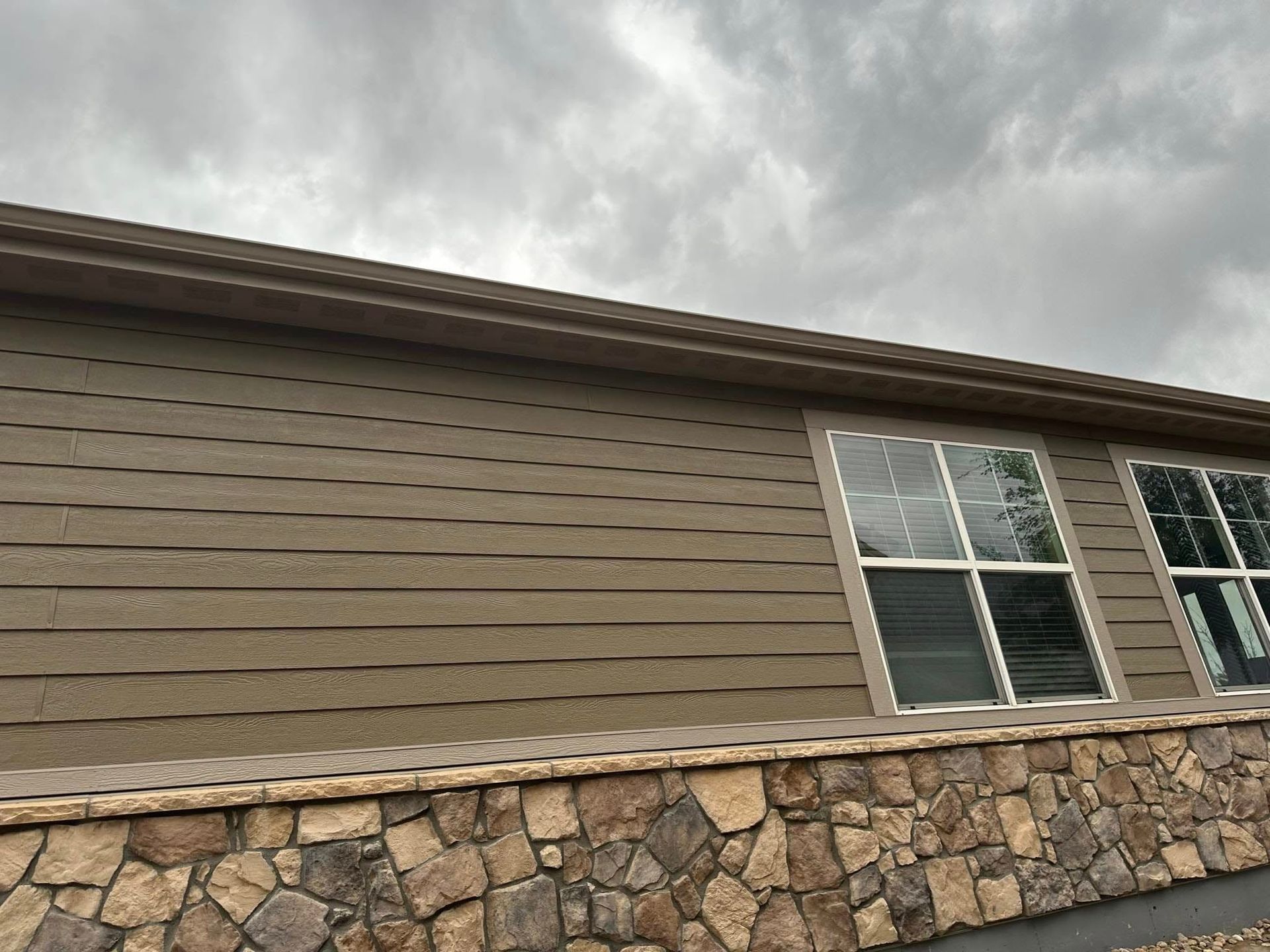 A house with a stone wall and a cloudy sky in the background.