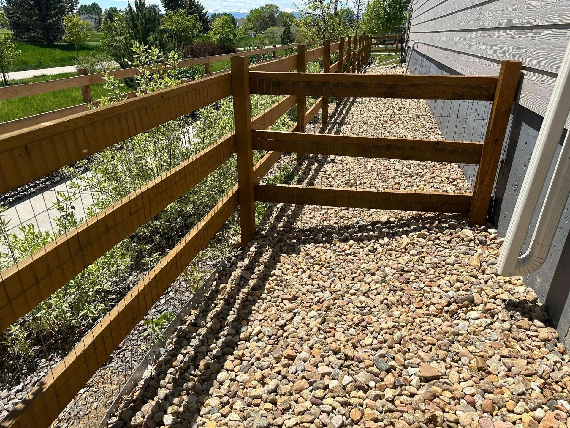 A wooden fence surrounds a gravel area next to a house.