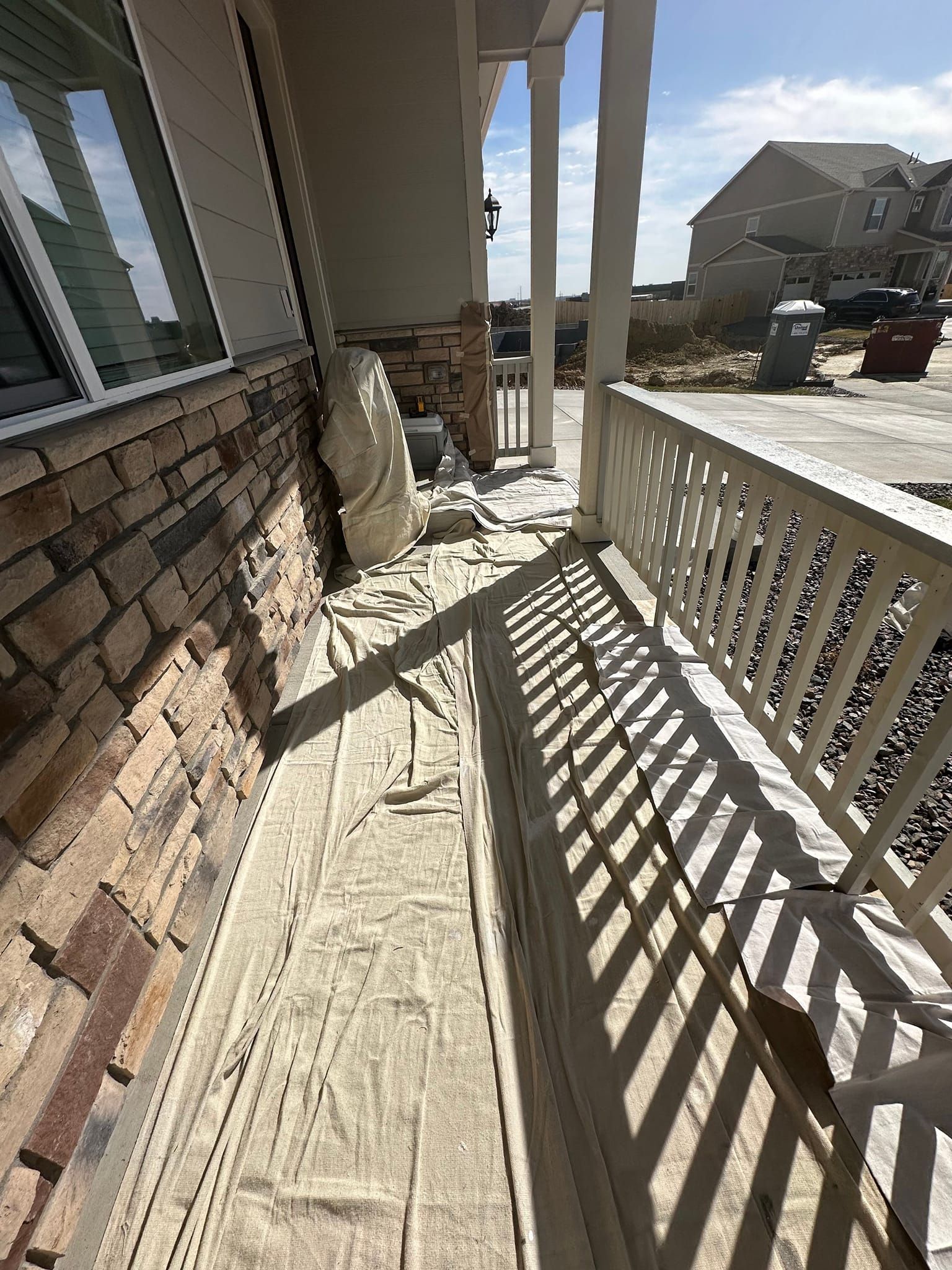 A porch with a brick wall and a white railing is being painted.