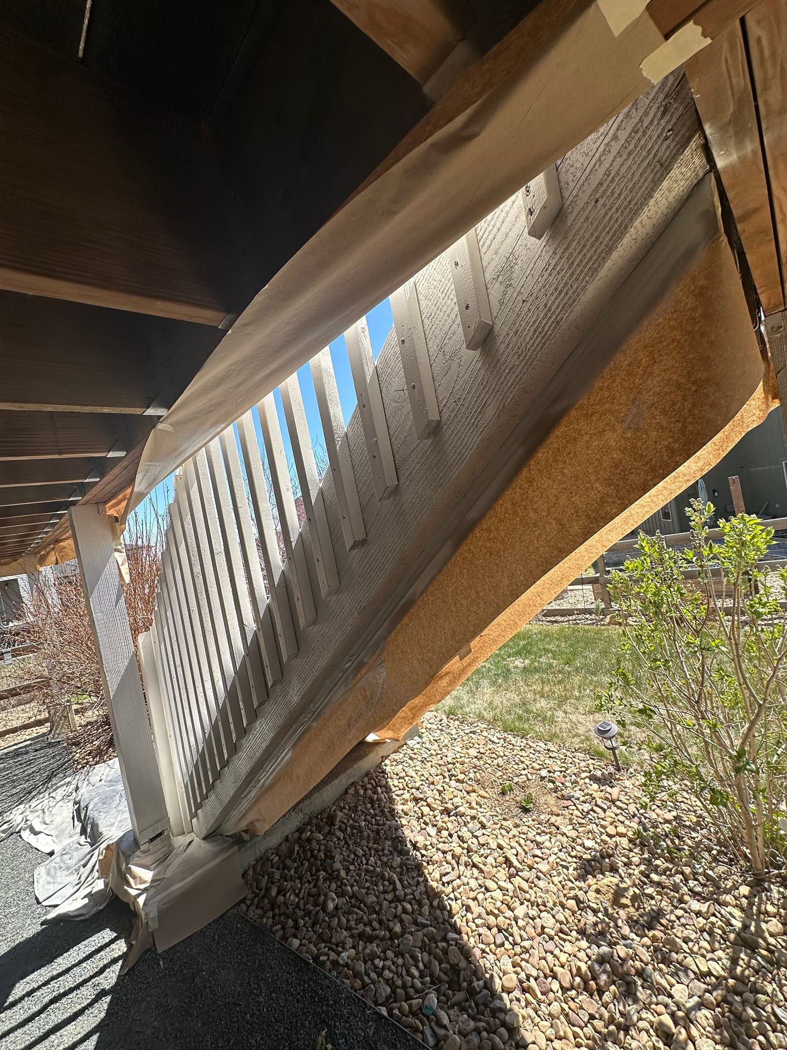 A white railing is sitting under a wooden deck.