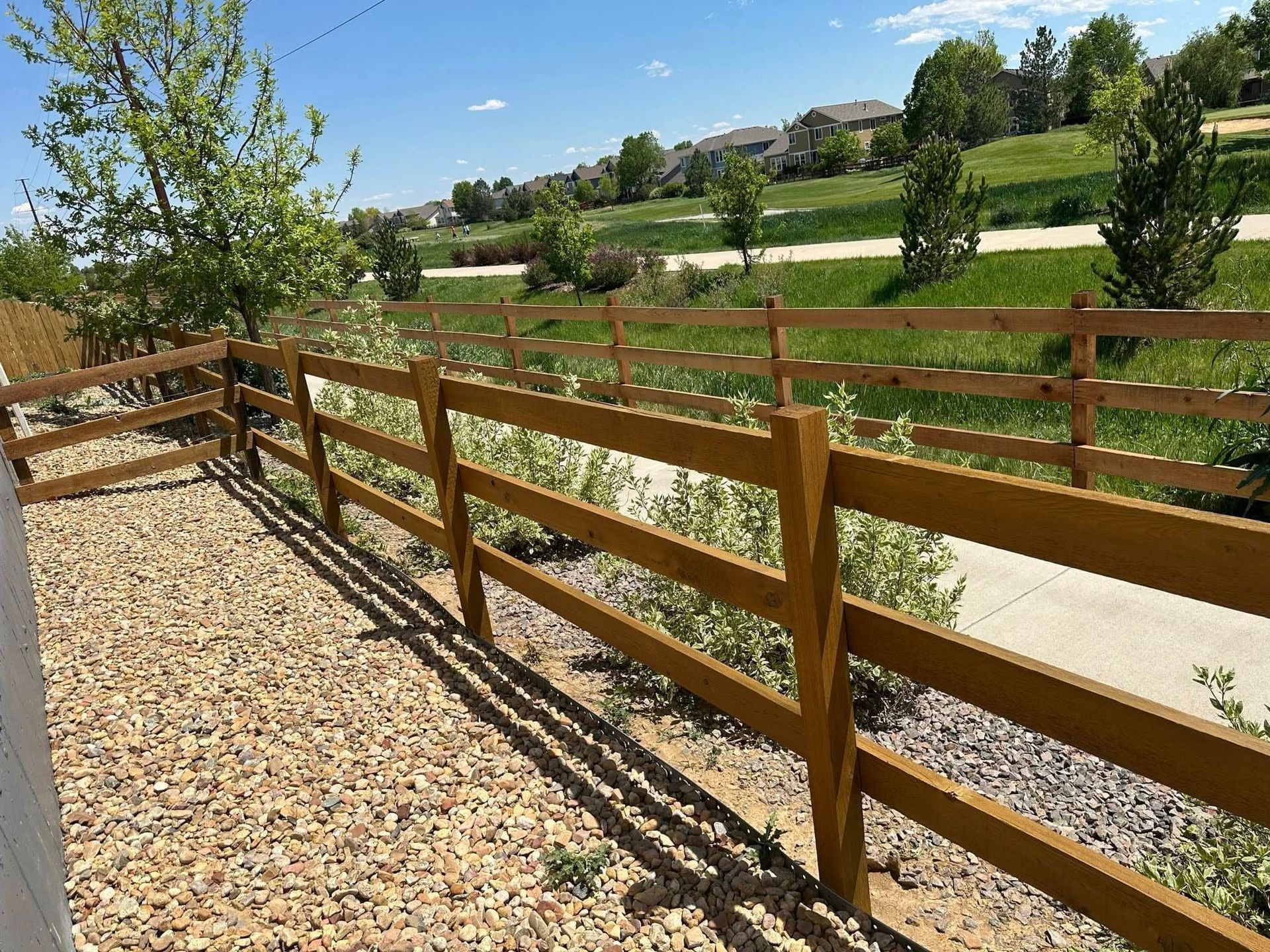 A wooden fence surrounds a gravel area with trees in the background.