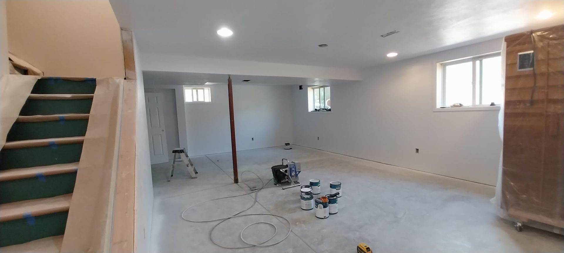 A basement with white walls and green stairs is being painted.