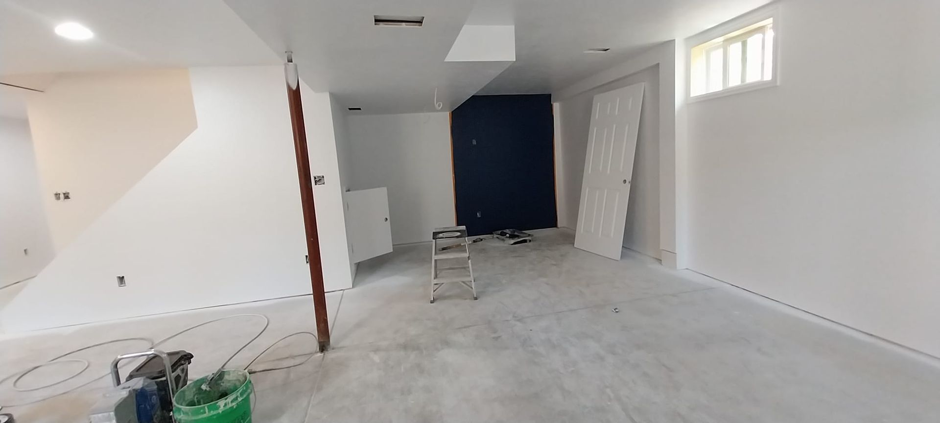 A room with white walls and a green bucket on the floor.