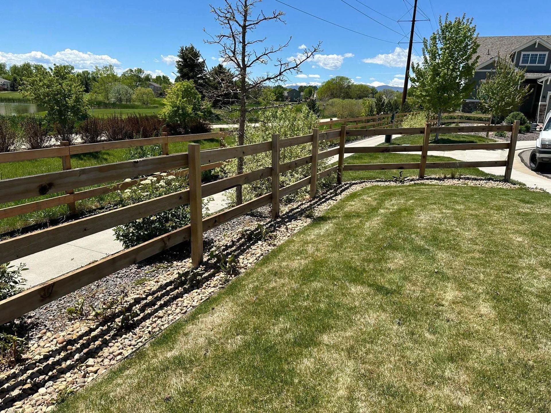 A wooden fence surrounds a lush green lawn in front of a house.