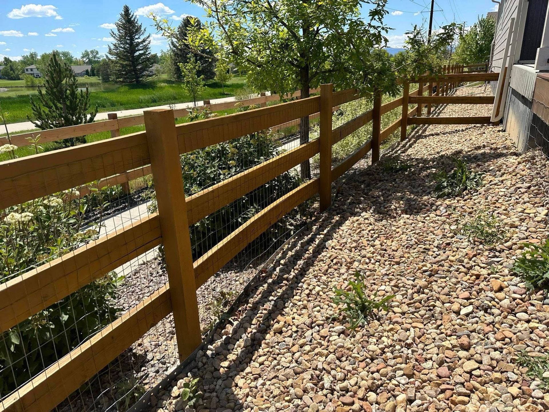 A wooden fence surrounds a gravel area next to a house.