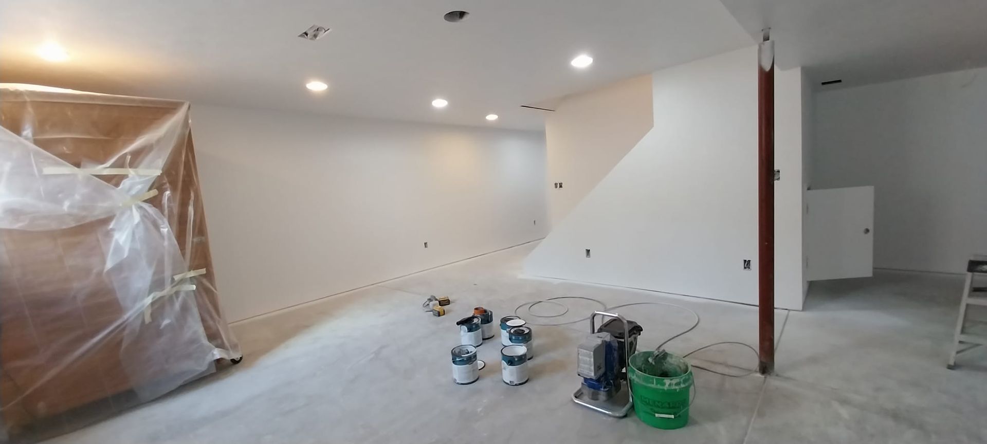 A large empty room with white walls and a green bucket of paint.