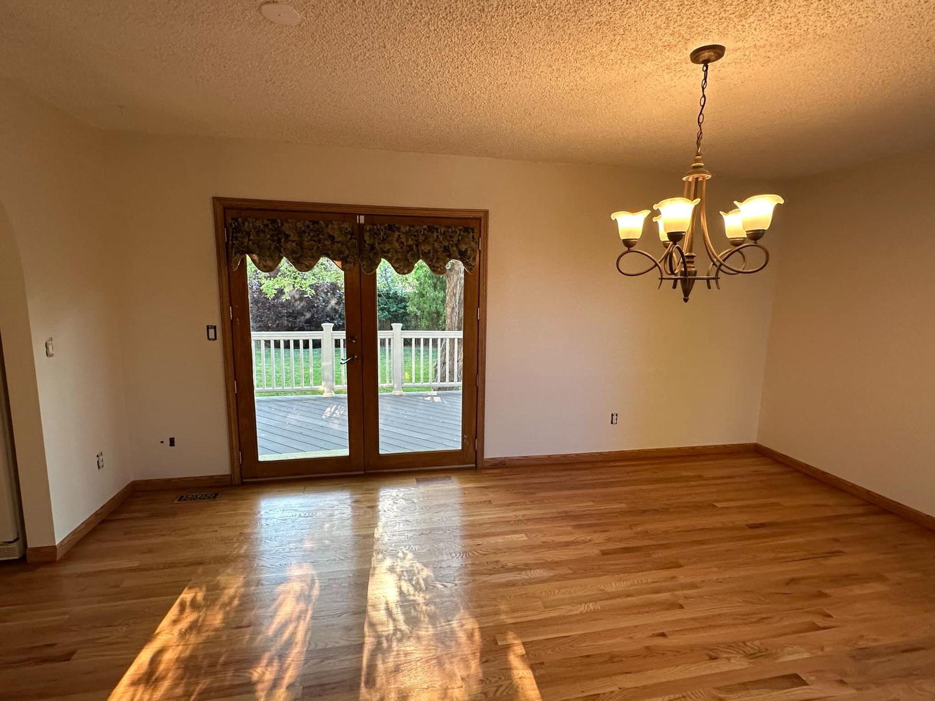 An empty dining room with hardwood floors and a chandelier hanging from the ceiling.