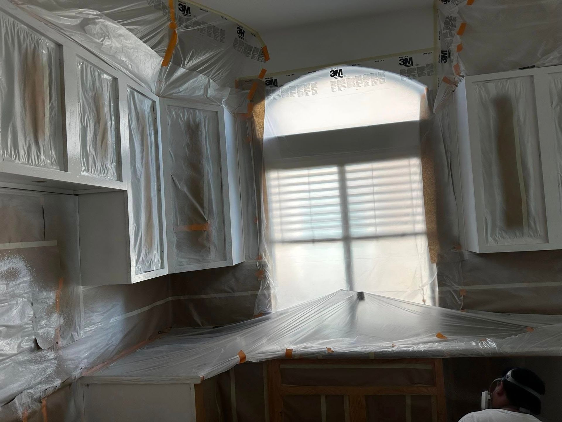 A kitchen with cabinets covered in plastic and a window.