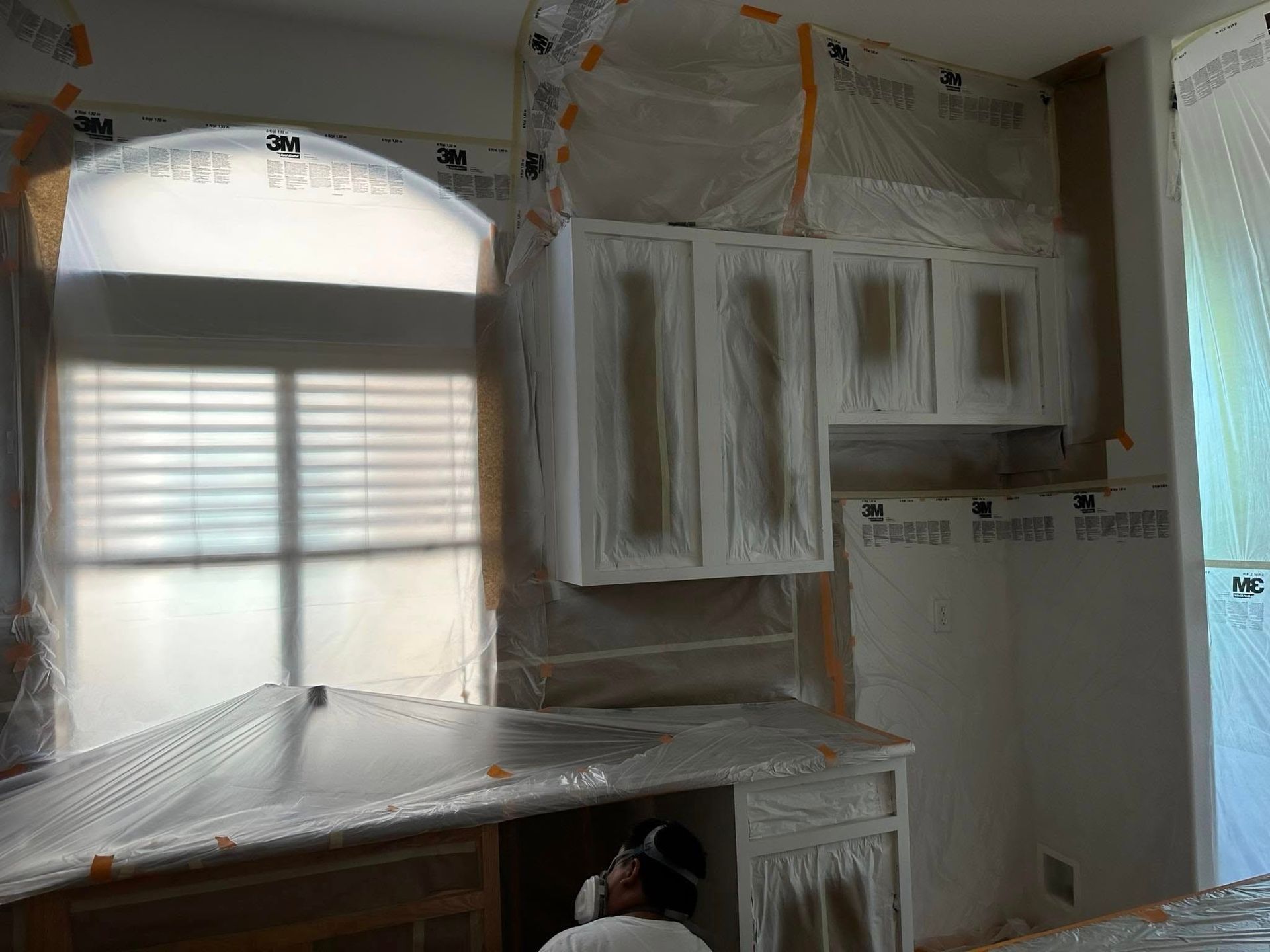 A man is painting a kitchen with plastic covering the cabinets.