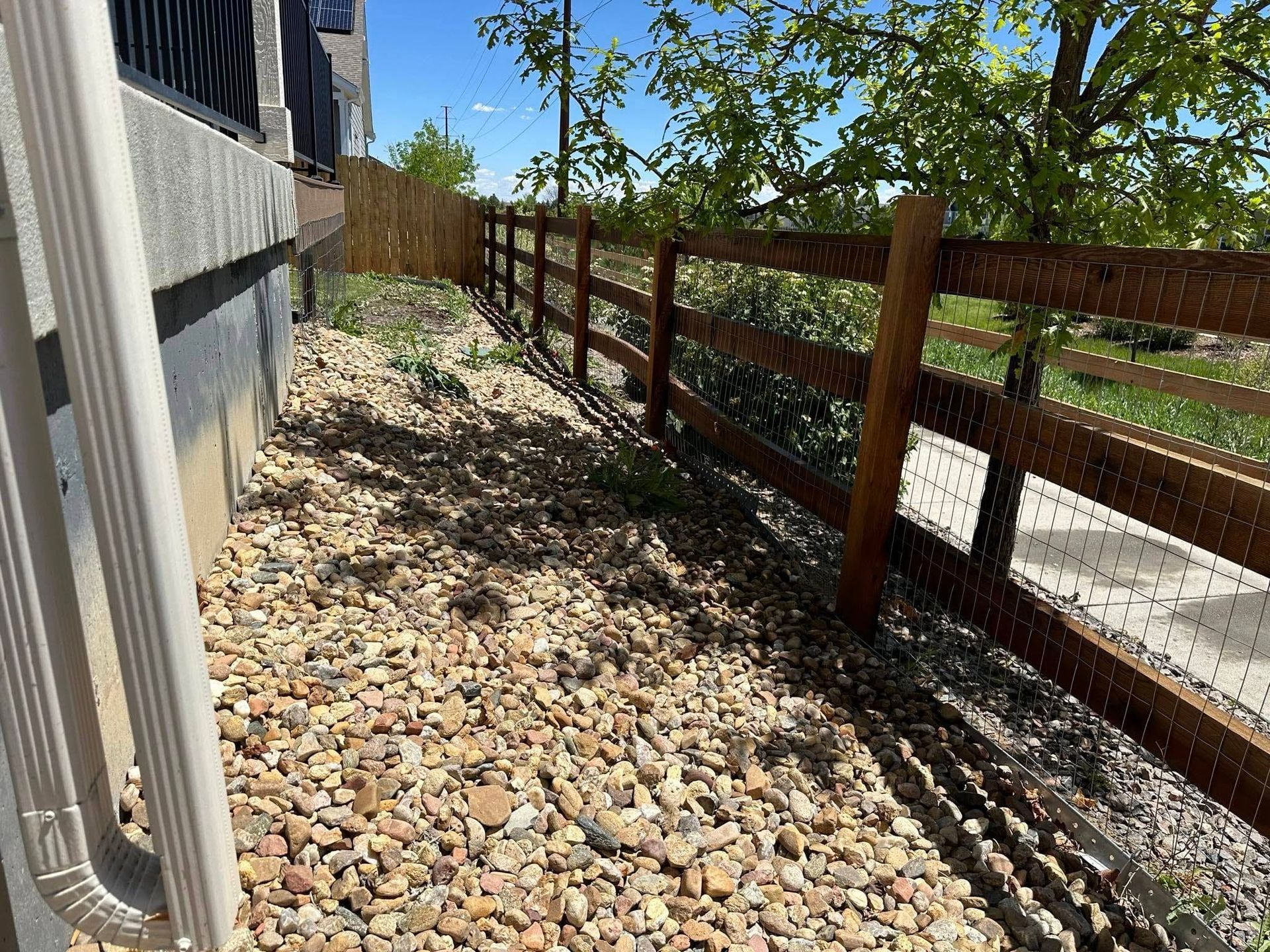 A wooden fence surrounds a gravel area next to a house.