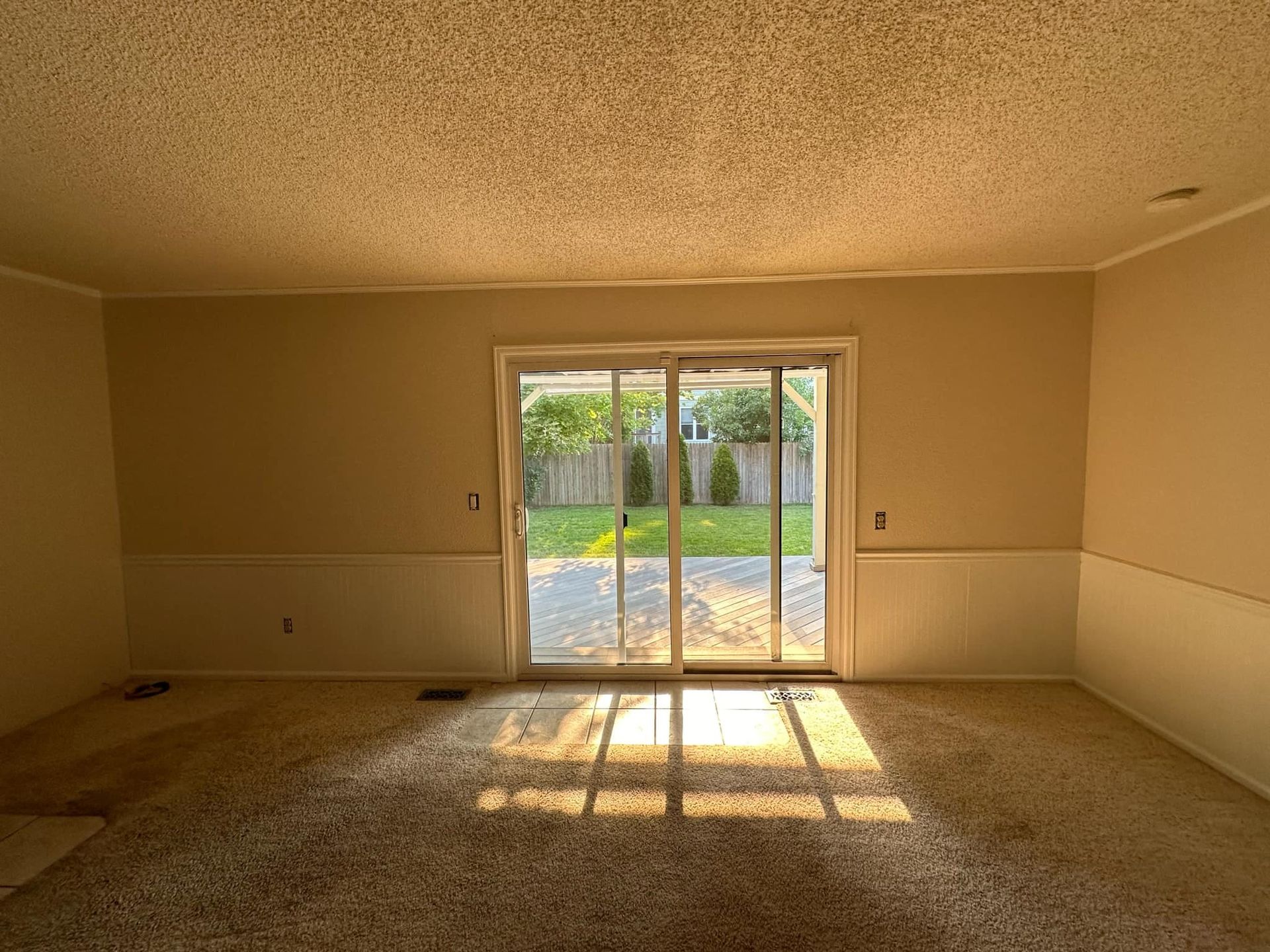 An empty living room with a sliding glass door leading to a backyard.
