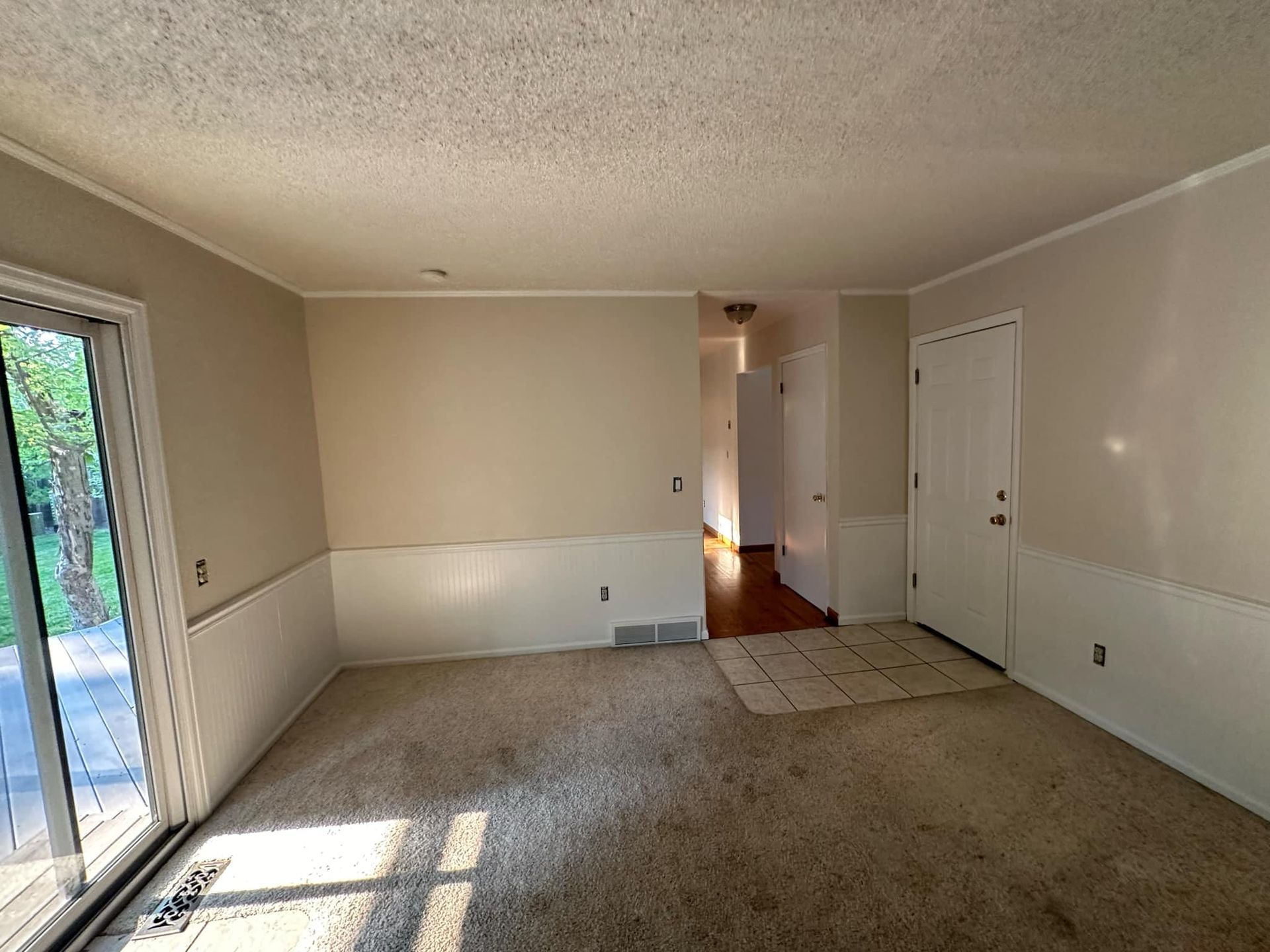 An empty living room with a sliding glass door and white walls.