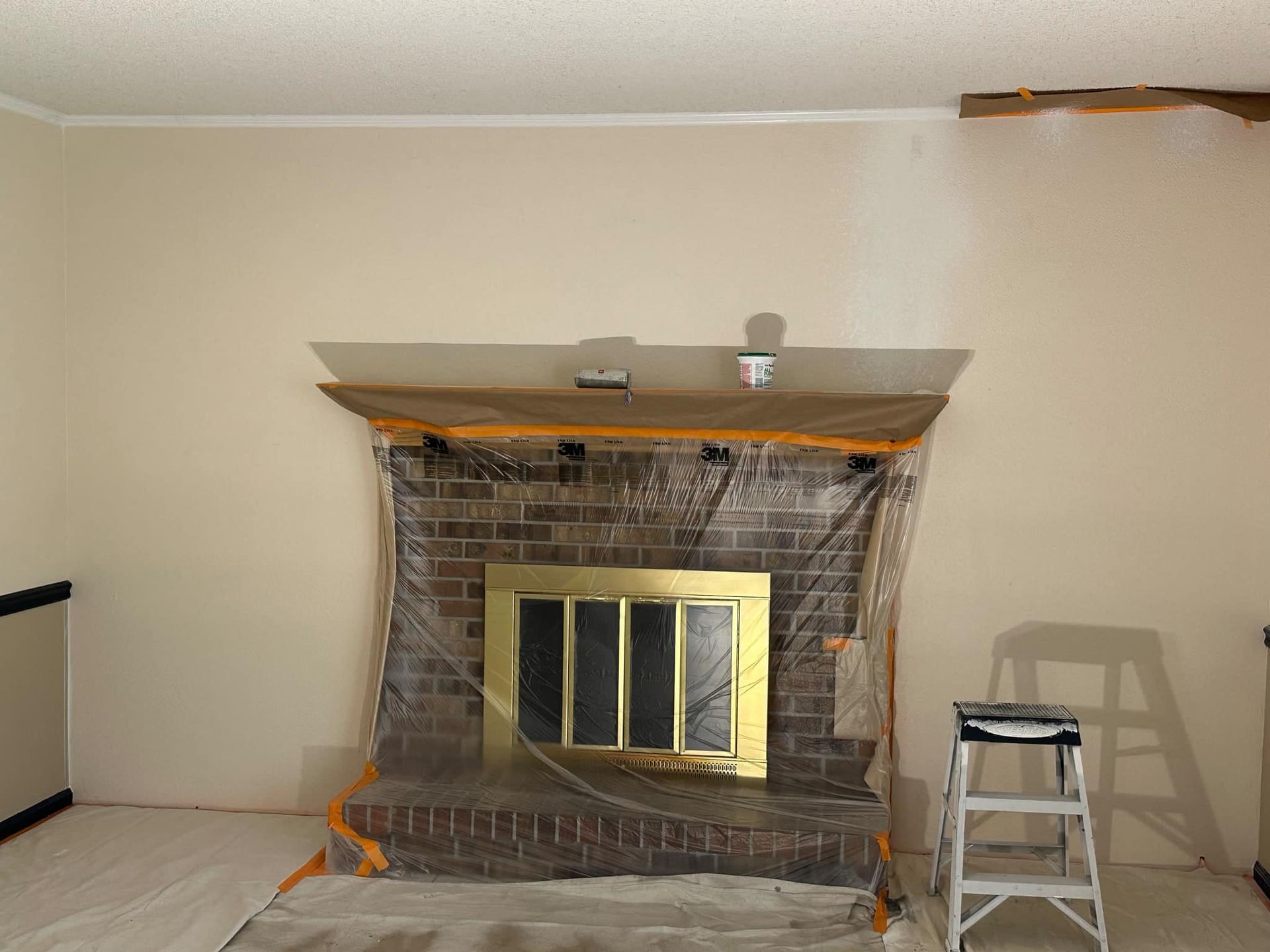 A living room with a fireplace covered in plastic and a ladder