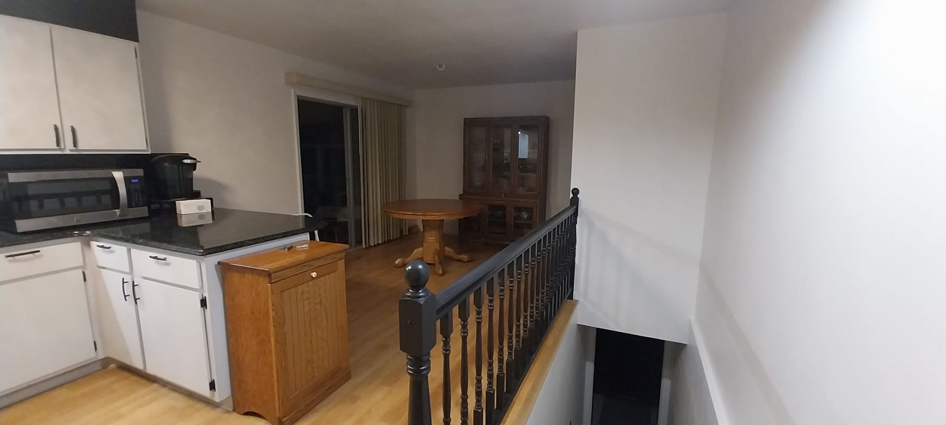 A kitchen with white cabinets , granite counter tops , a microwave and a table.