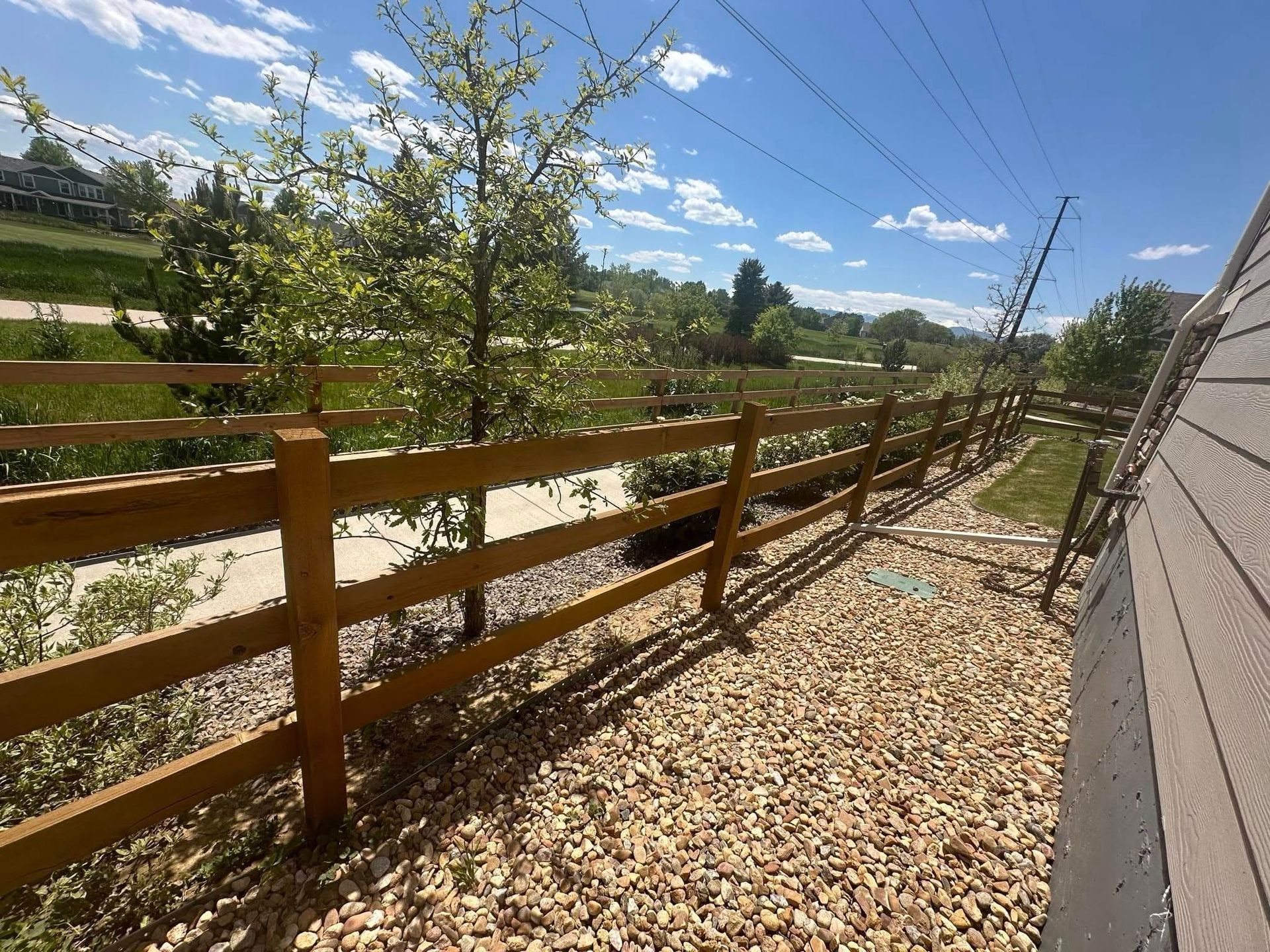 A wooden fence surrounds a gravel area next to a house.