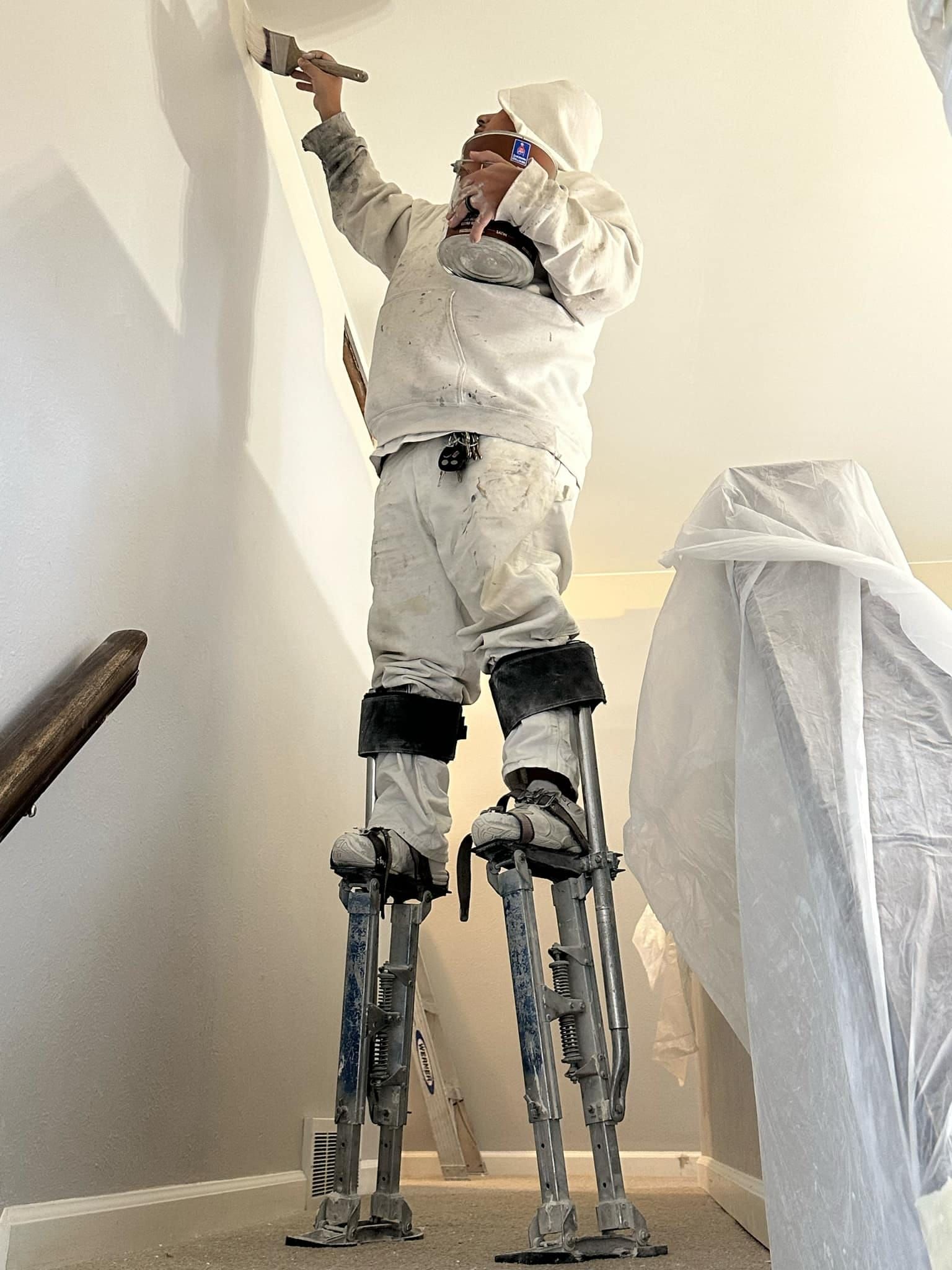 A man is standing on stilts painting a wall.