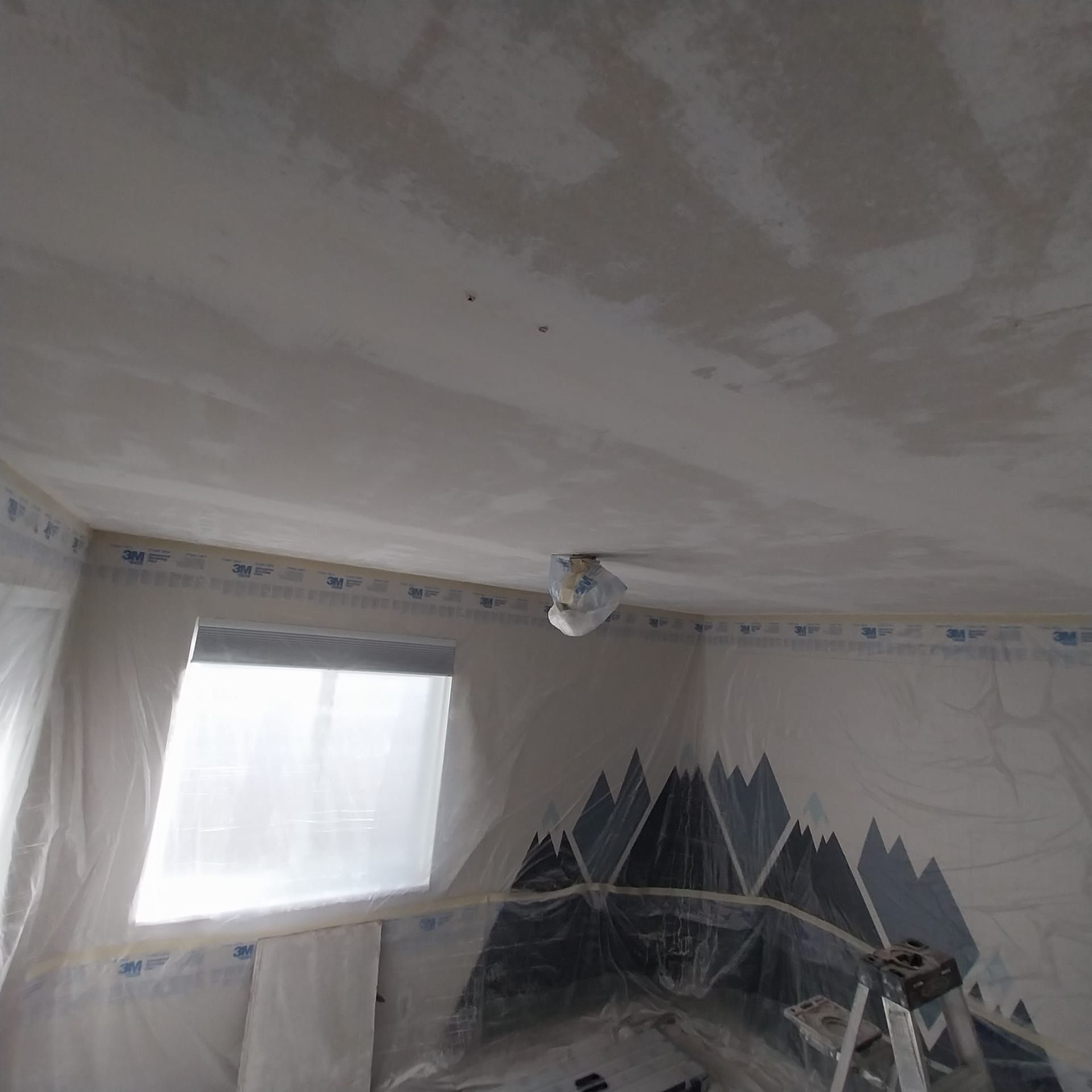 A room with a ceiling fan and a window covered in plastic.