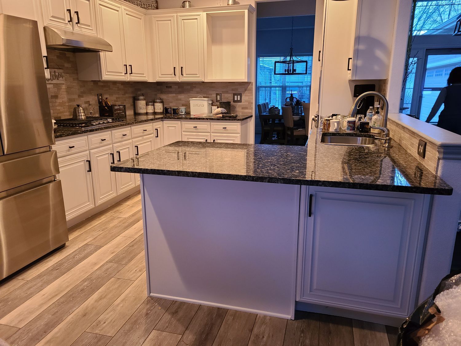 A kitchen with white cabinets , granite counter tops , stainless steel appliances and a large island.