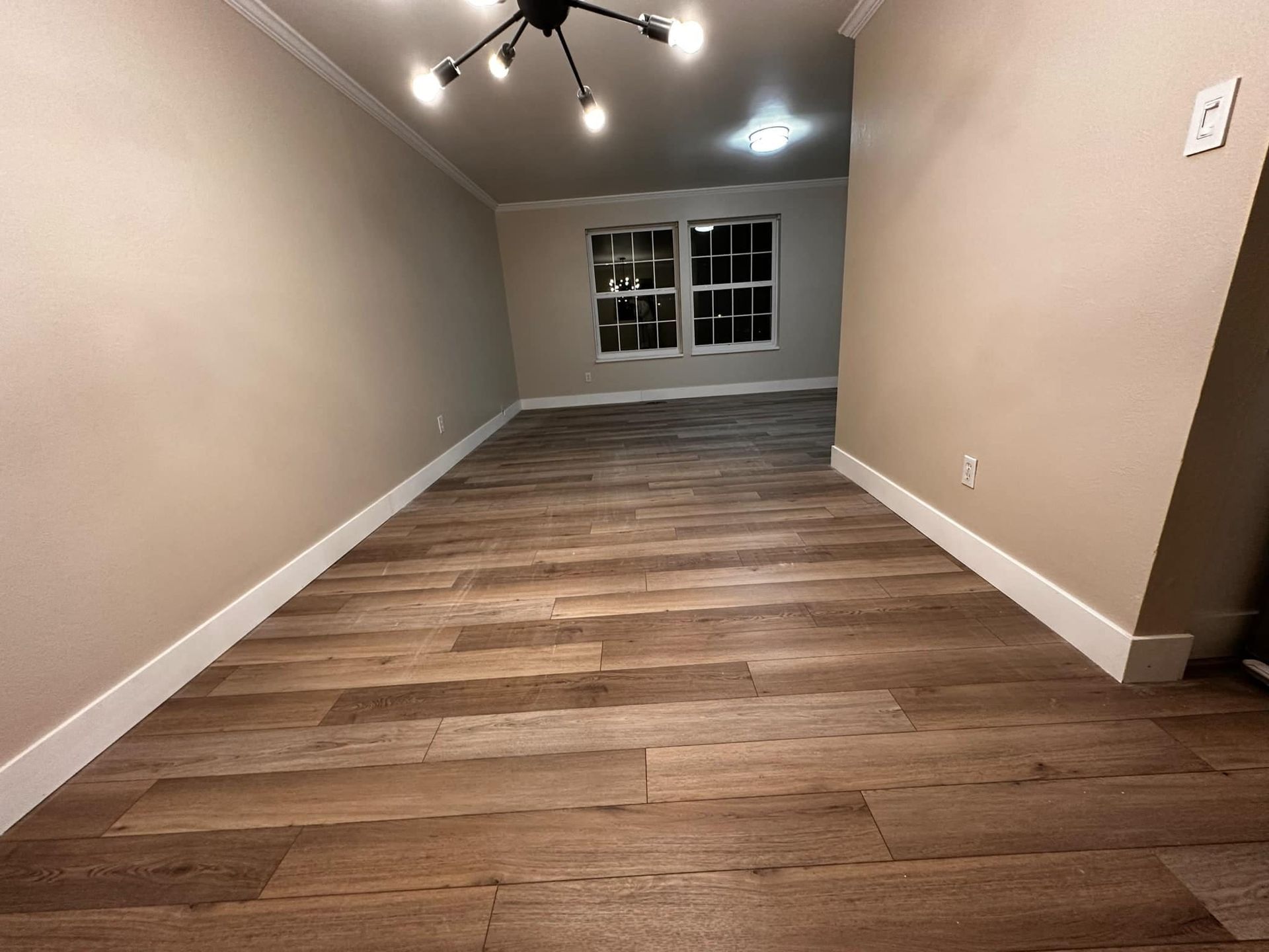 An empty living room with hardwood floors and a chandelier.