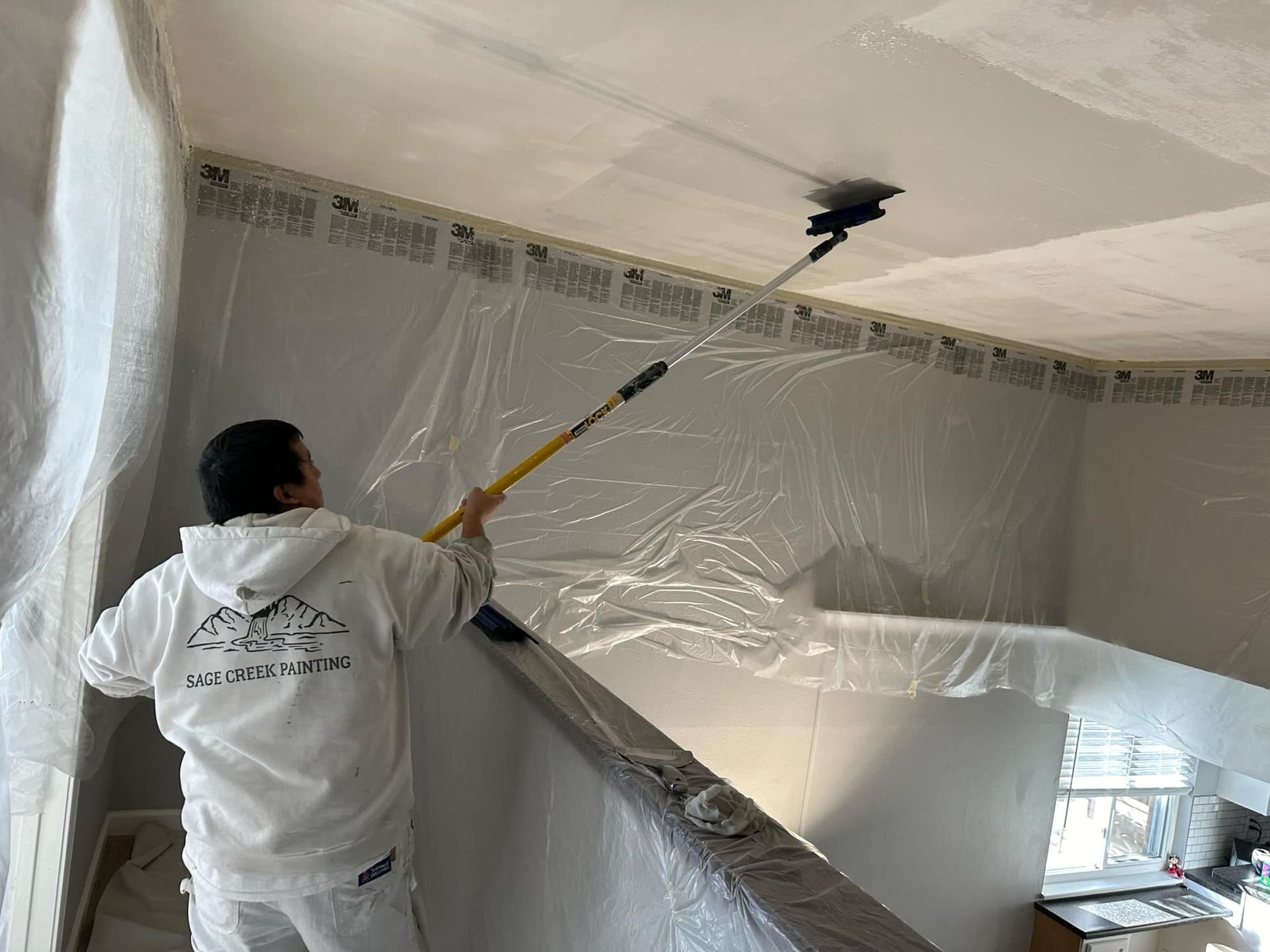 A man is painting the ceiling of a room with a roller.