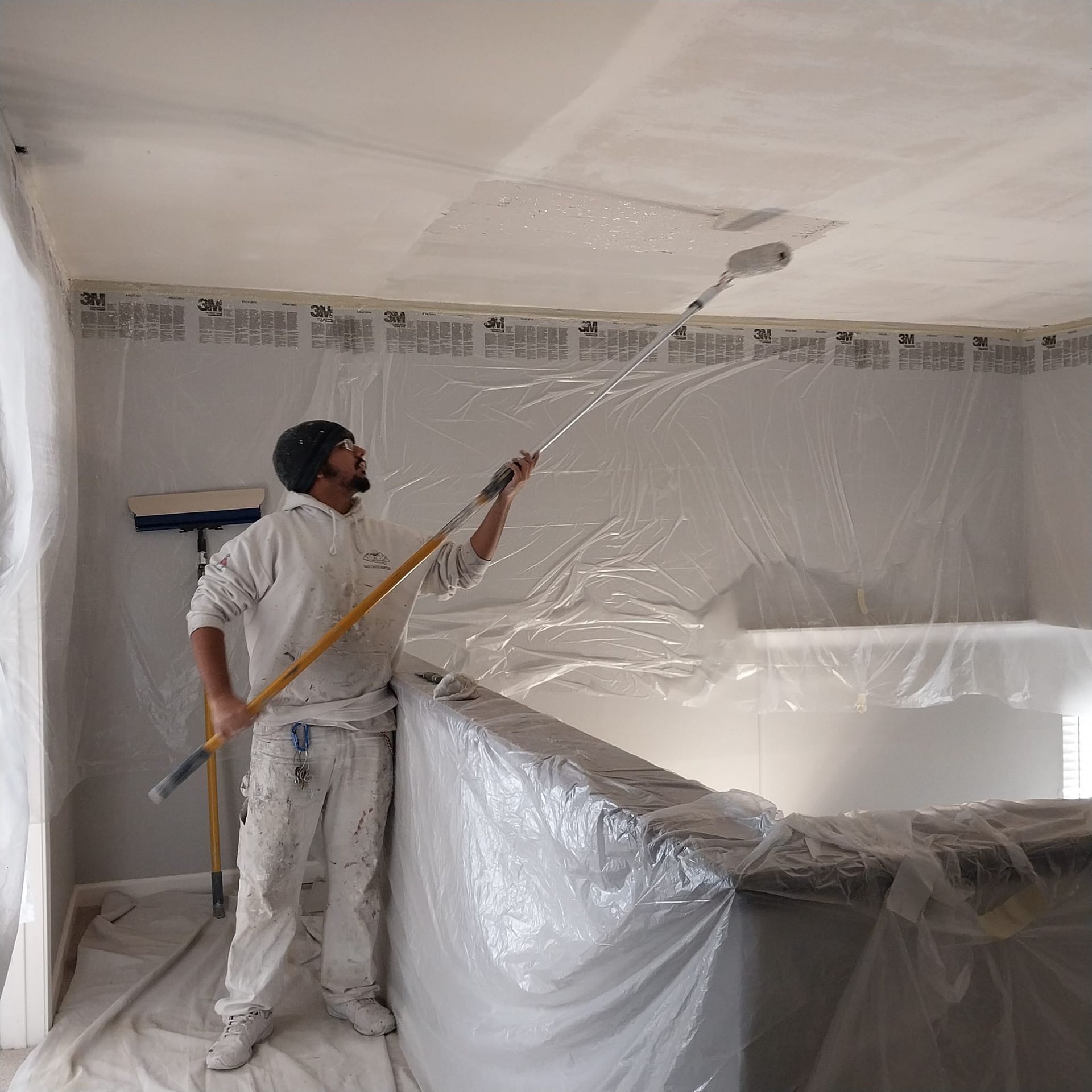 A man is painting the ceiling of a room with a roller.
