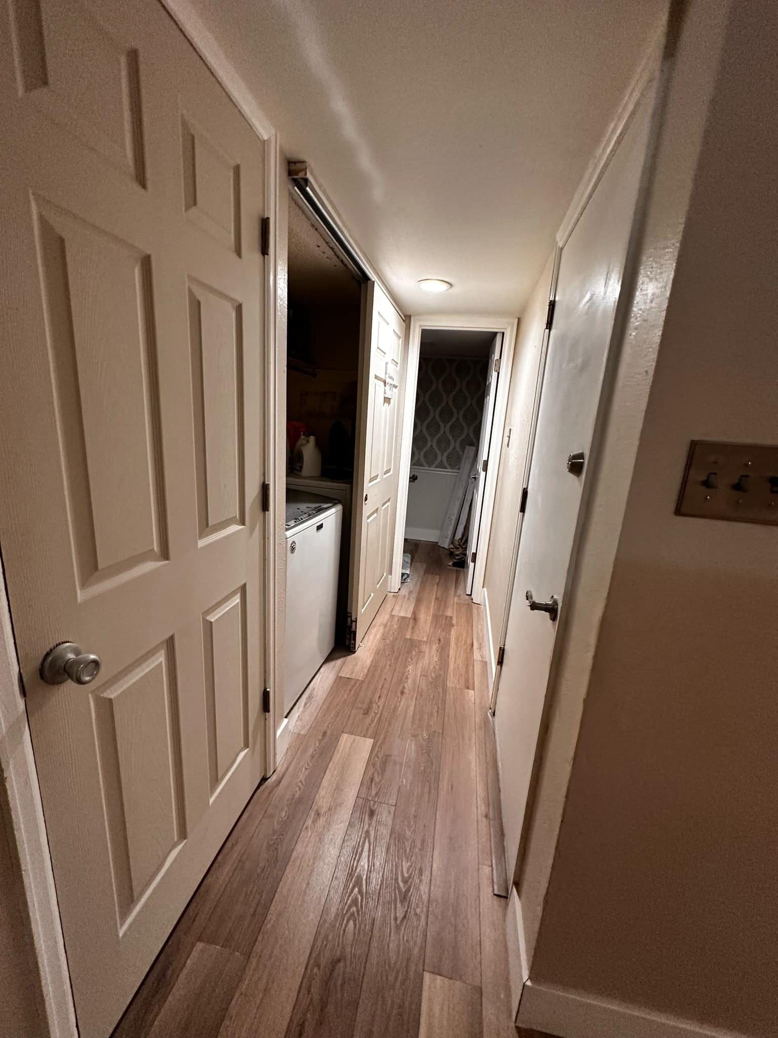 A long hallway with hardwood floors and white doors leading to a kitchen.