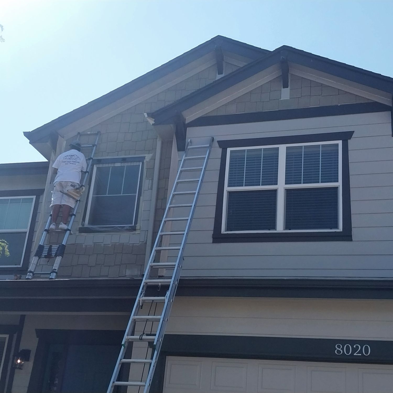 A man is painting the side of a house with a ladder.