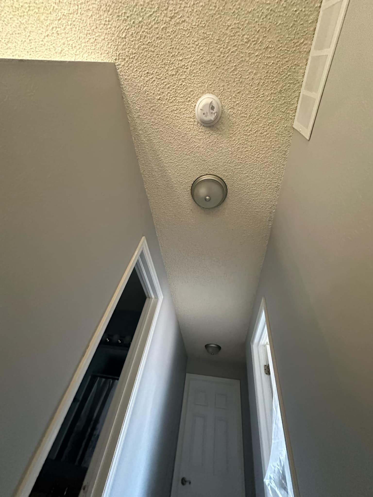 A hallway with a smoke detector on the ceiling and a door.