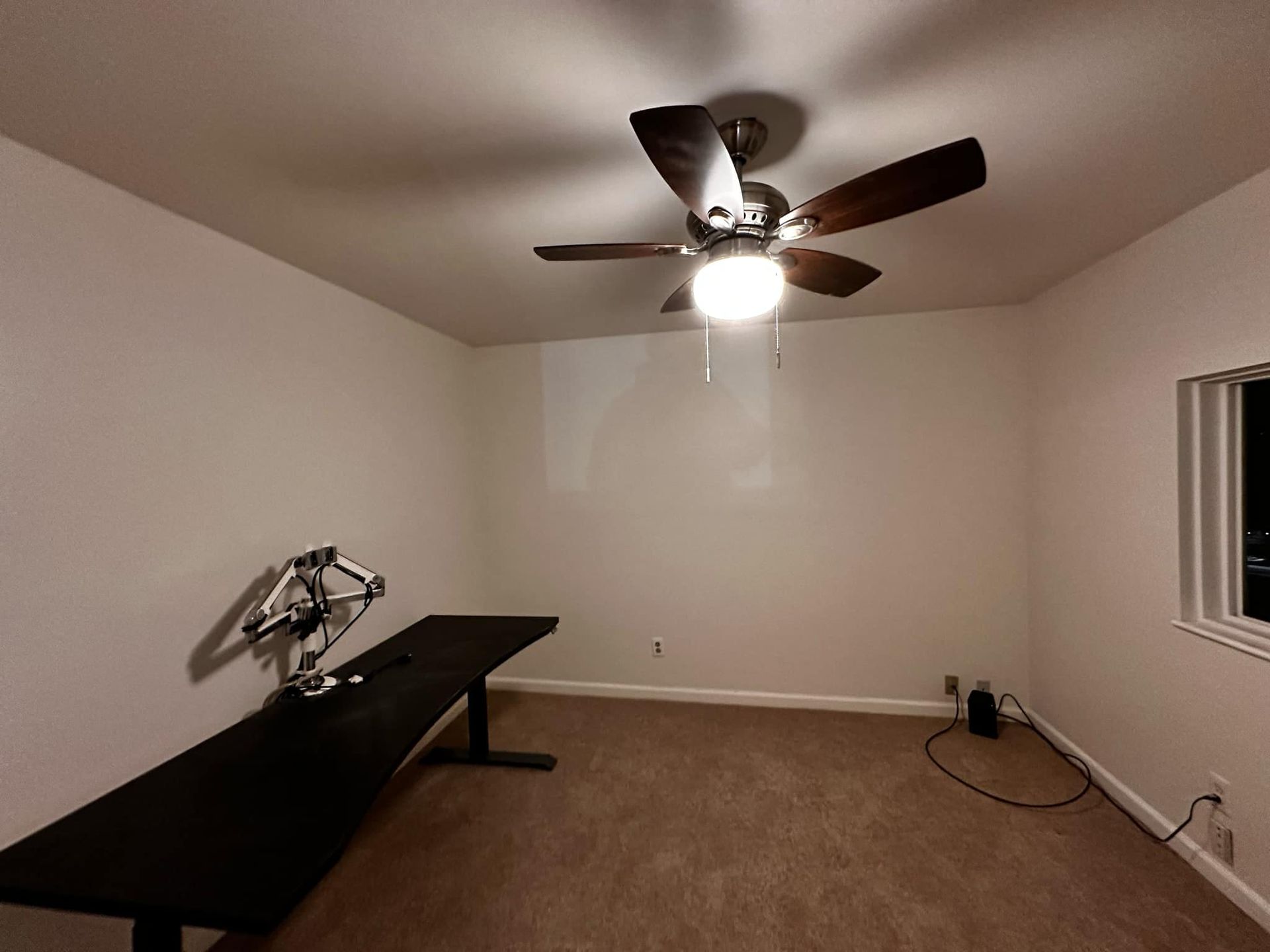 An empty room with a ceiling fan and a desk.