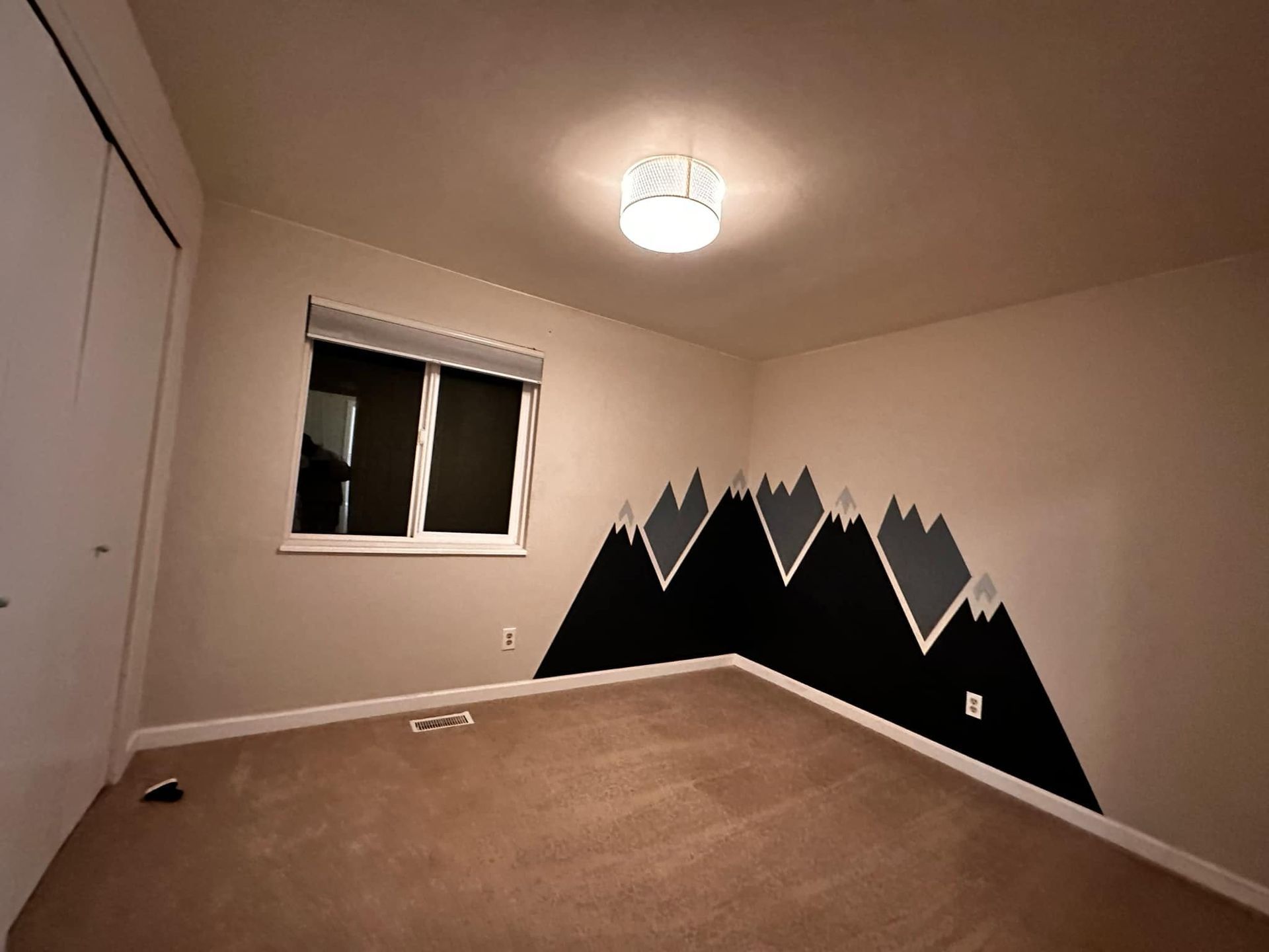 An empty bedroom with a painting of mountains on the wall.
