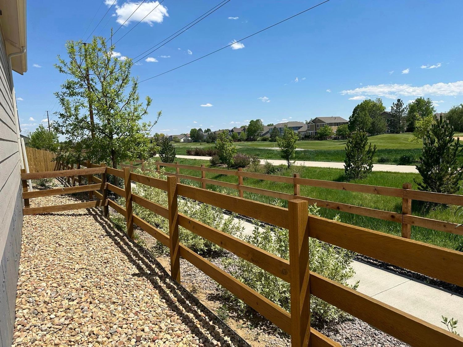 A wooden fence surrounds a gravel area next to a house.