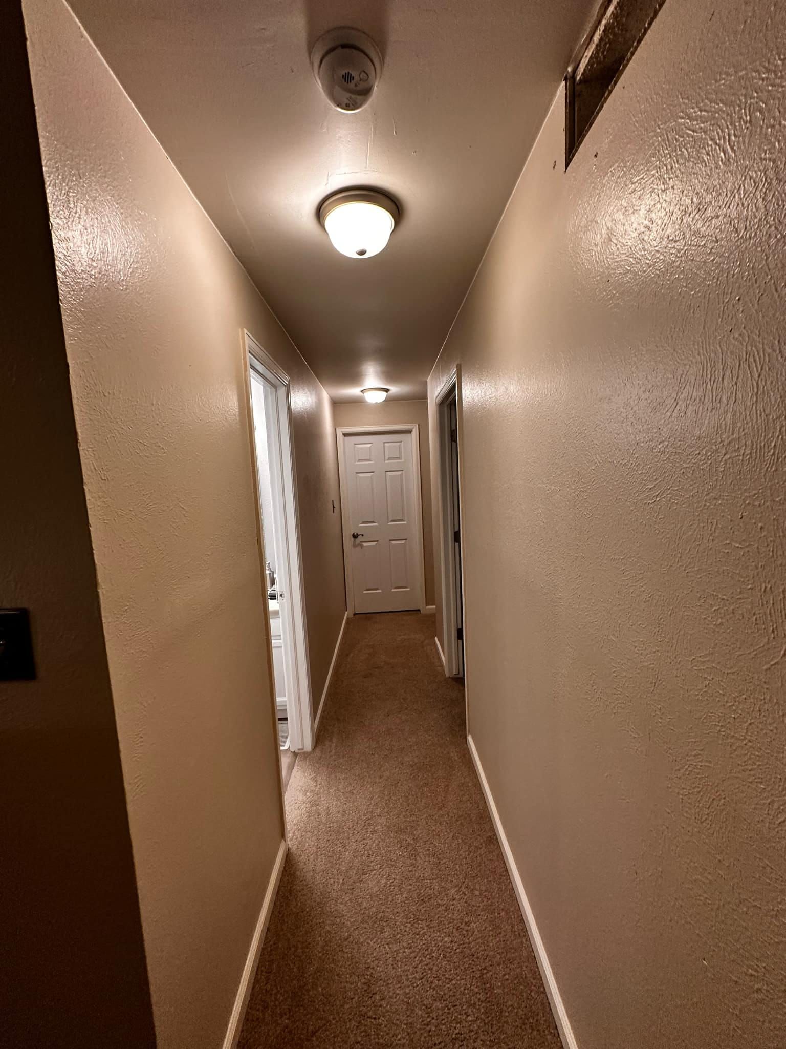A long hallway with a light on the ceiling and a door.