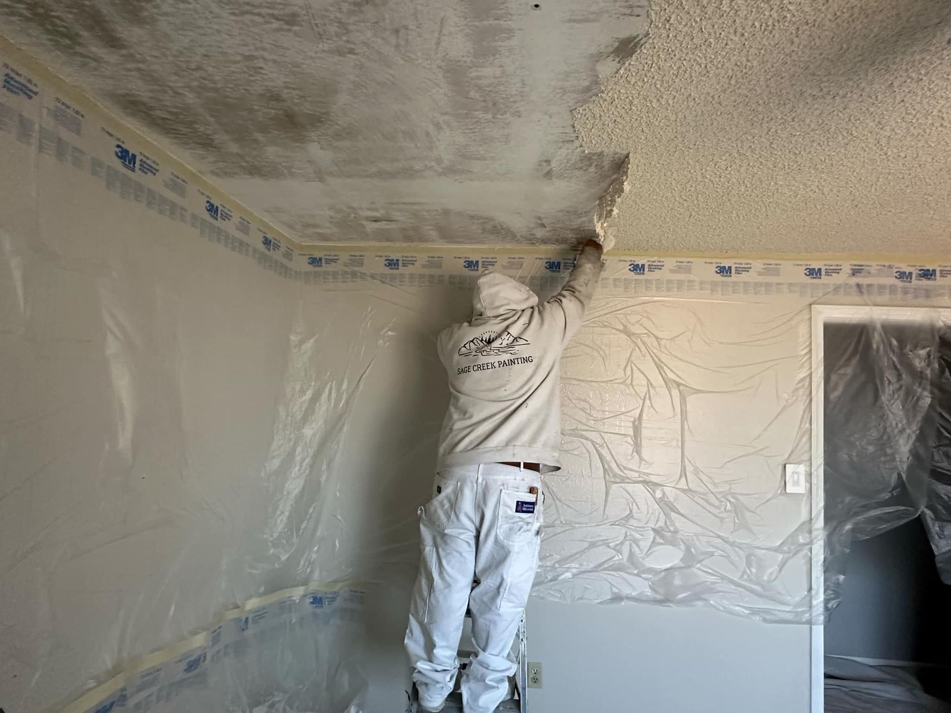 A man is standing on a ladder in a room painting the ceiling.