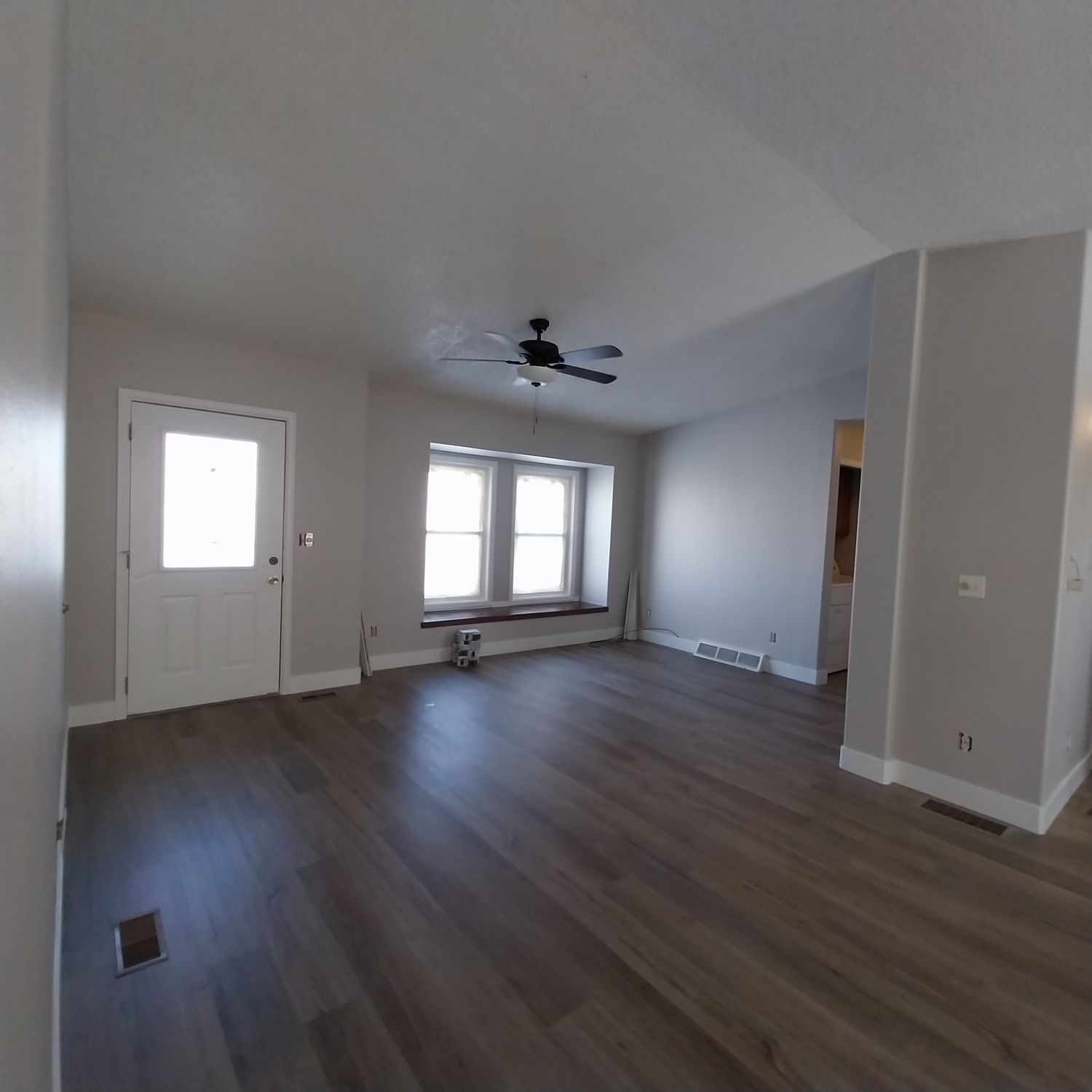 An empty living room with hardwood floors and a ceiling fan