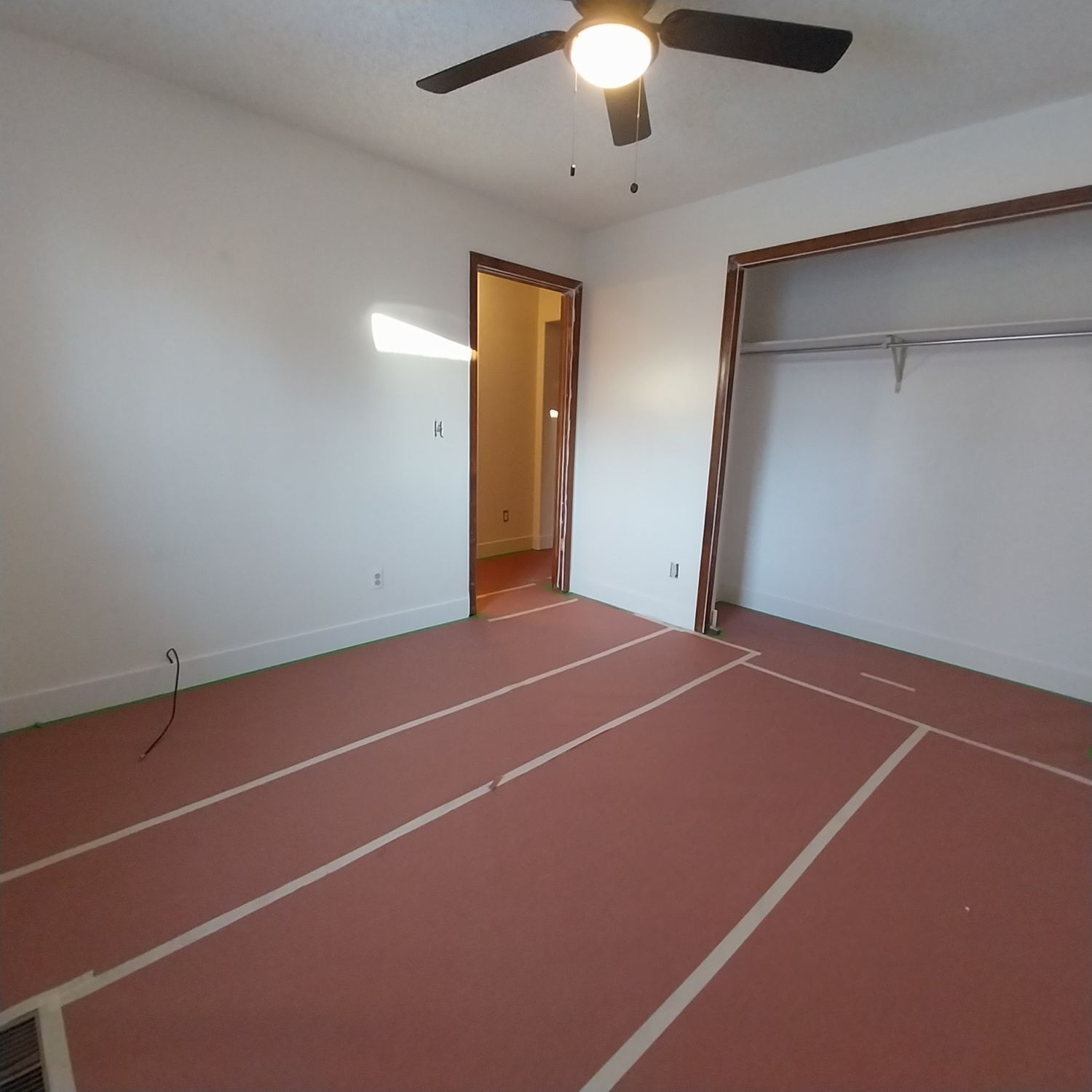 An empty room with a ceiling fan and a red floor