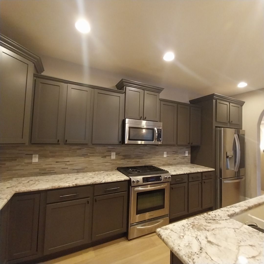 A kitchen with gray cabinets , stainless steel appliances and granite counter tops.