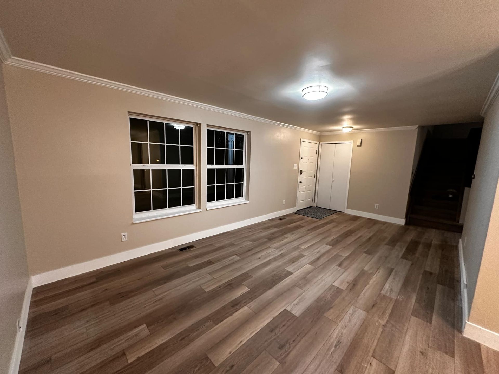 An empty living room with hardwood floors and two windows.