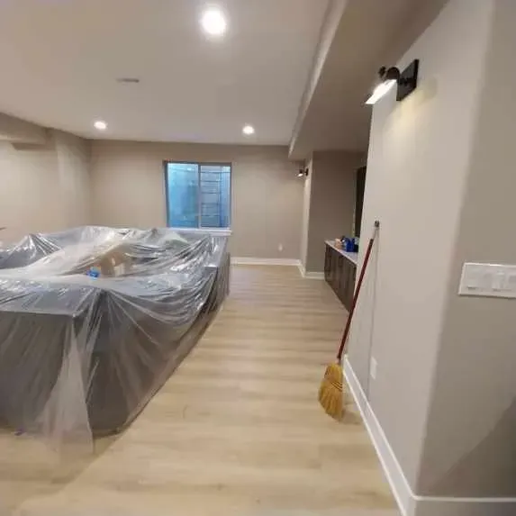 A living room with a couch covered in plastic and a broom.