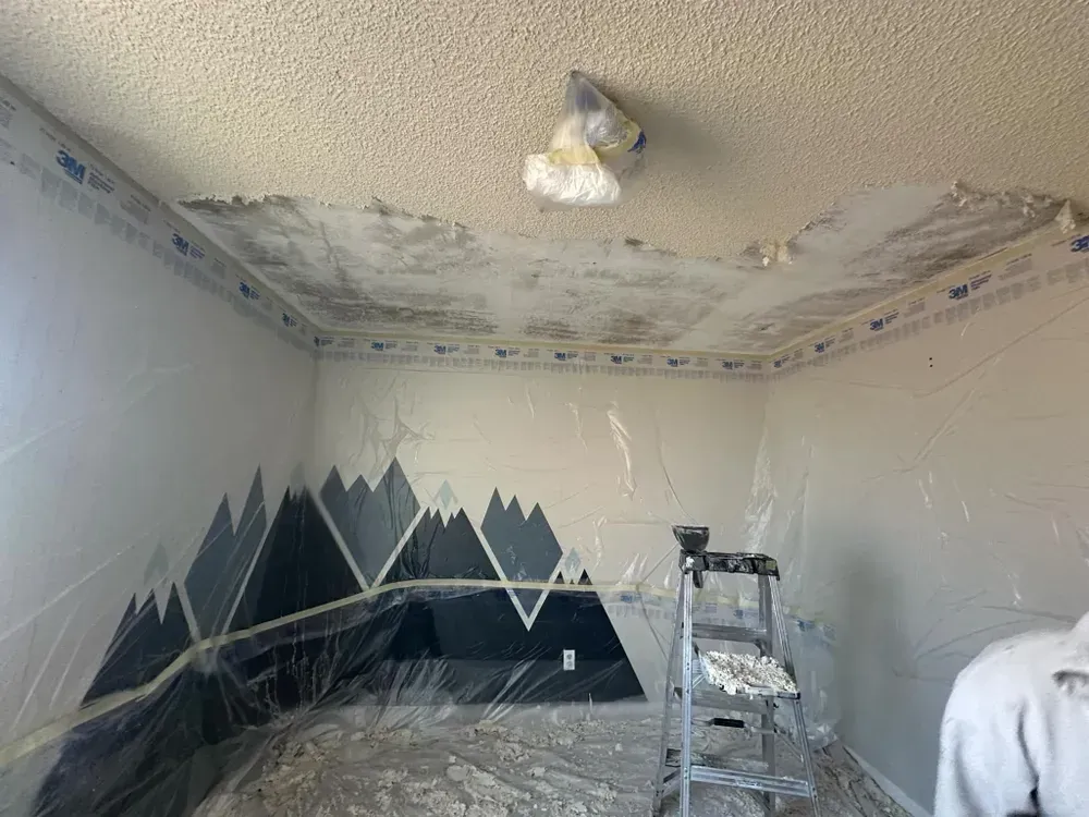 A room with a ladder and a painting of mountains on the wall.