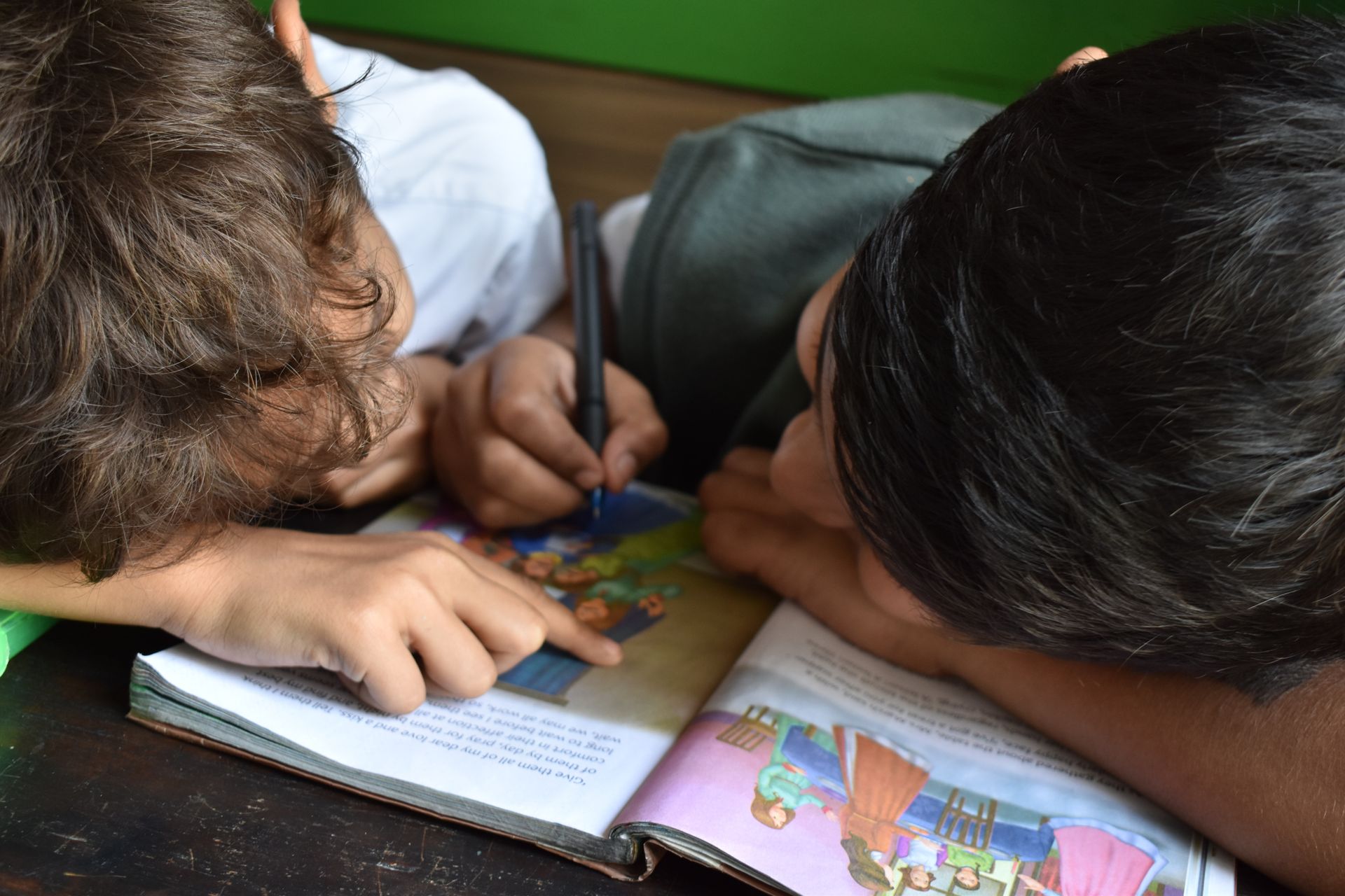 Two children are laying on the floor reading a book together