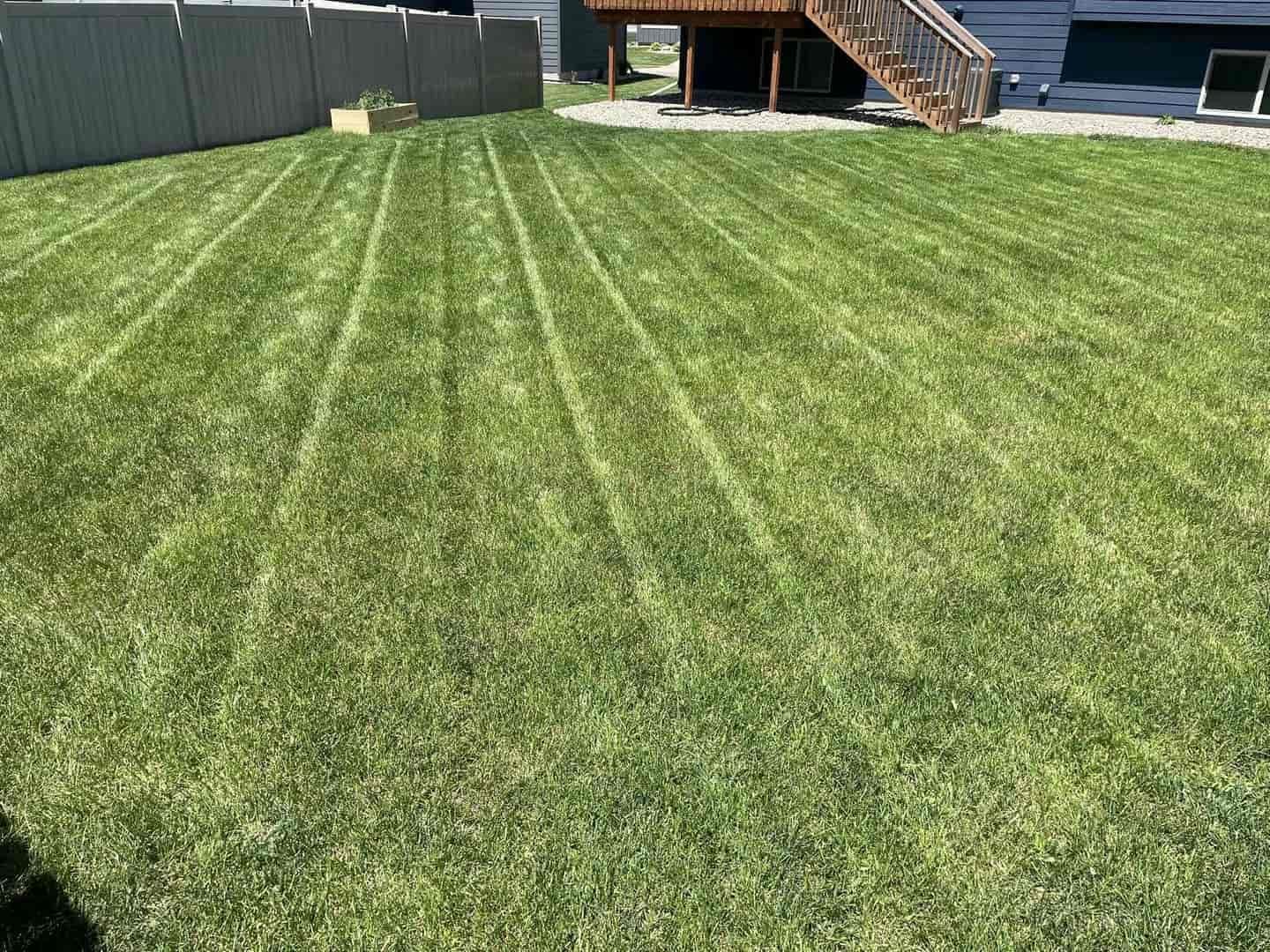 Green lawn with straight mower lines, fence, and a deck.