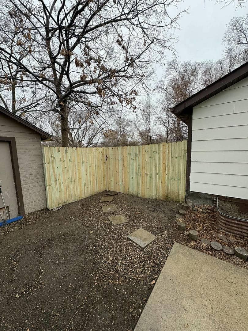 Wooden fence built between two buildings in an outdoor area covered in gravel and a concrete walkway.