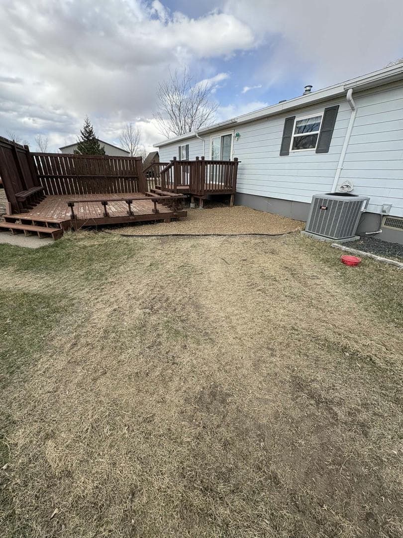 Brown wooden deck next to a light-colored house; patchy yard, overcast sky.
