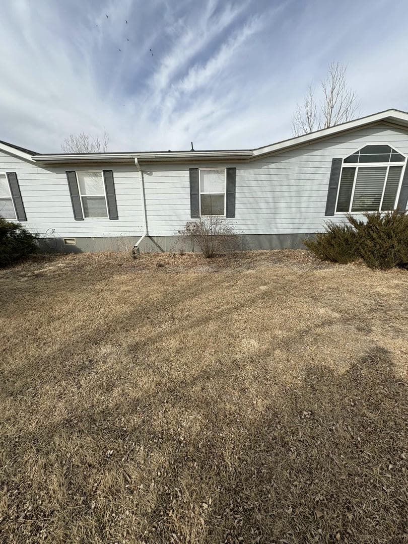 Exterior of a light-colored house with dark shutters, dry brown grass, and a cloudy sky.