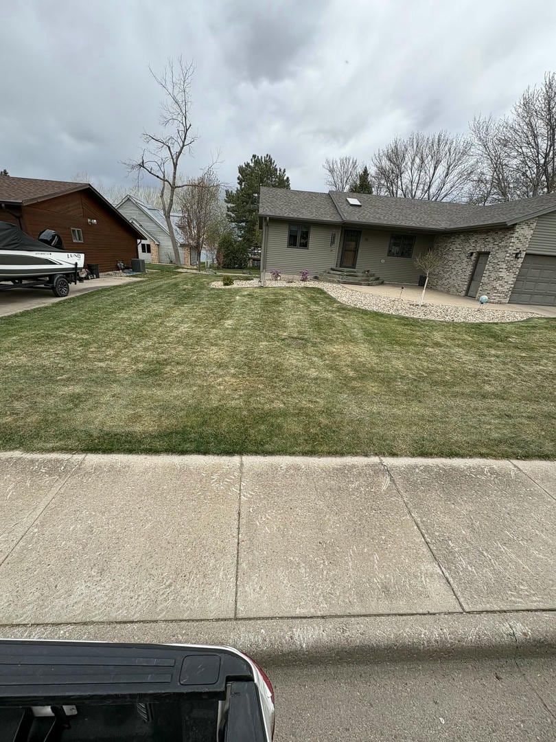 A residential lawn in front of a house, sidewalk in foreground, overcast sky.