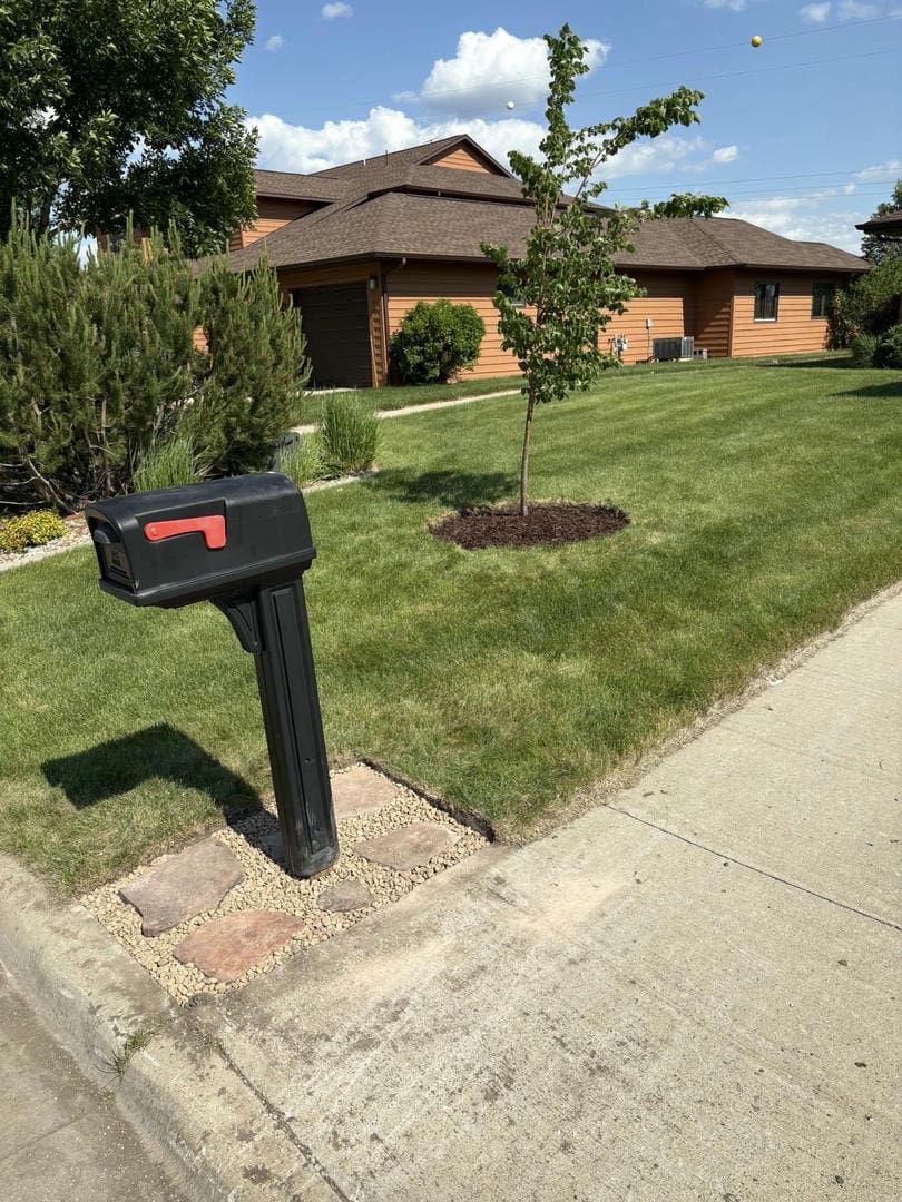 Black mailbox on a brick base next to a sidewalk and green lawn, with a house in the background.