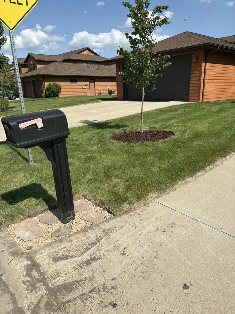 Black mailbox on concrete sidewalk with green lawn and house in the background.