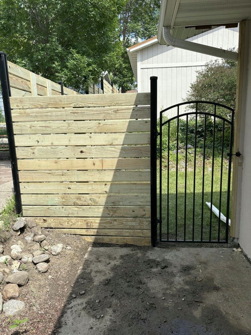 Wooden retaining wall with a black metal gate and steps leading upward.