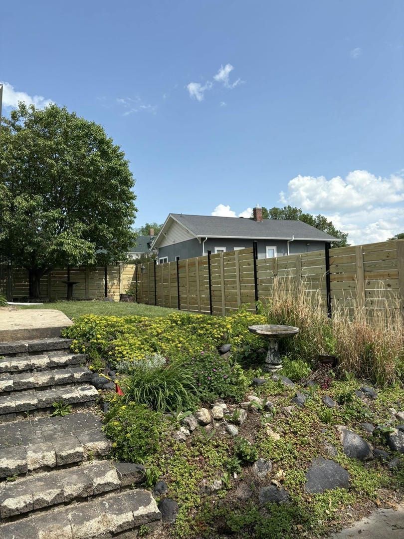 Stone steps lead up to a backyard with a new wooden fence, tree, and house under a blue sky.