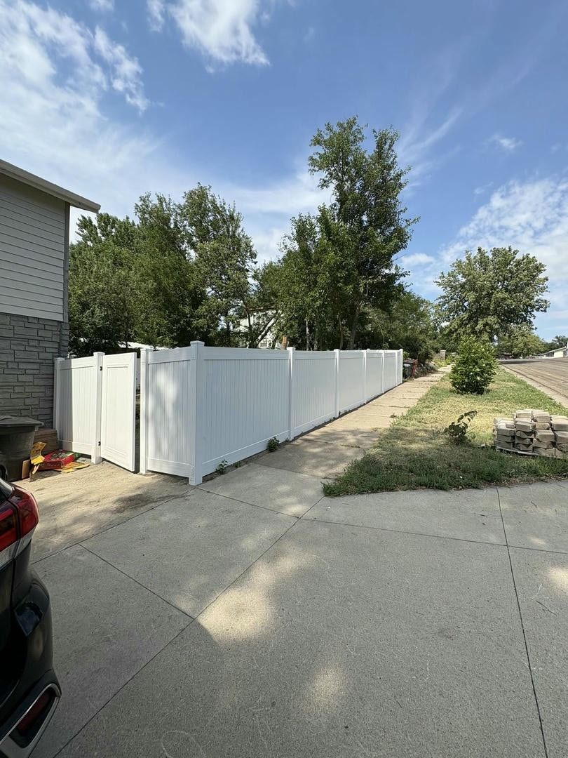 White vinyl fence along a concrete driveway, under a partly cloudy sky.